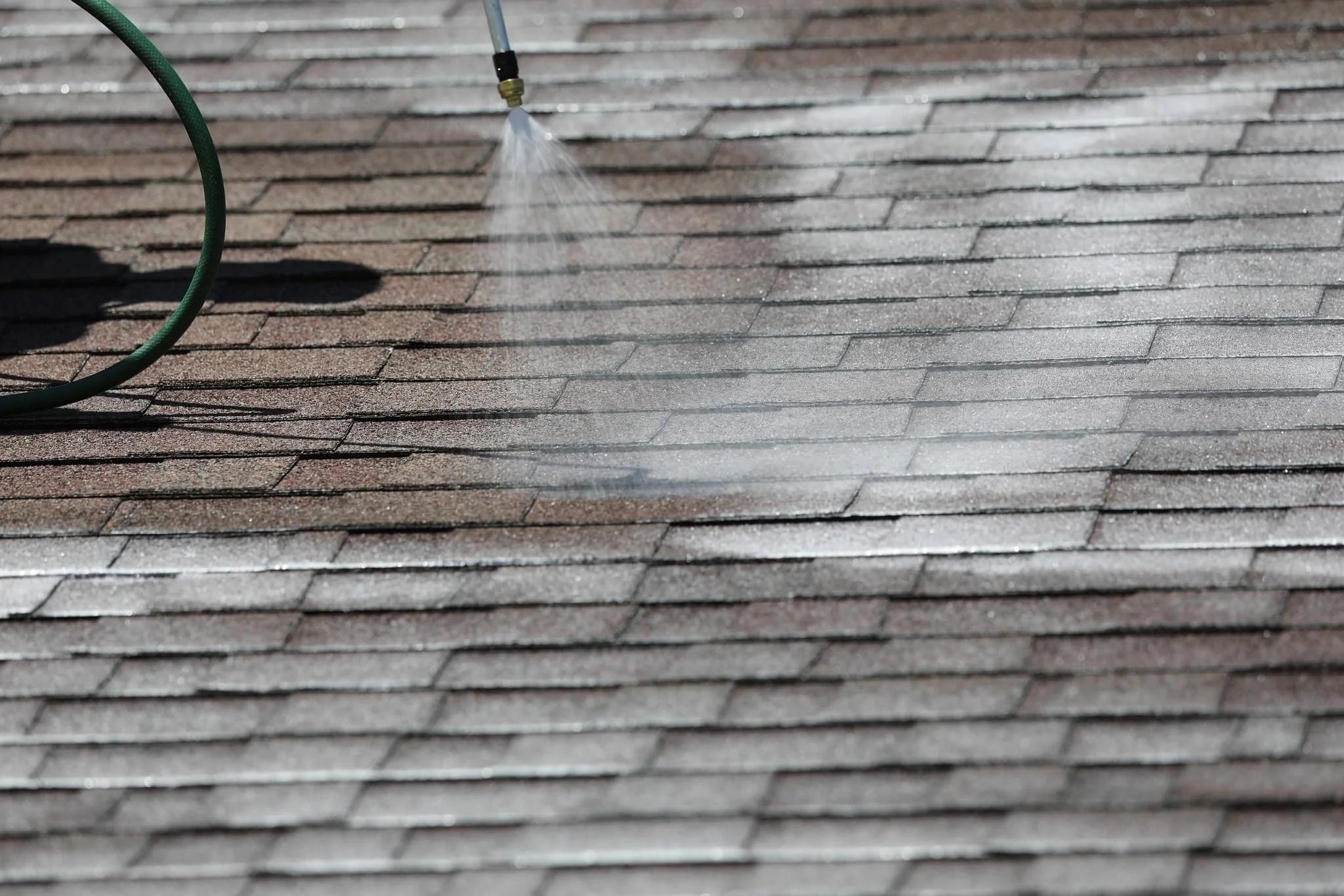 A garden hose spraying water on a shingled roof.