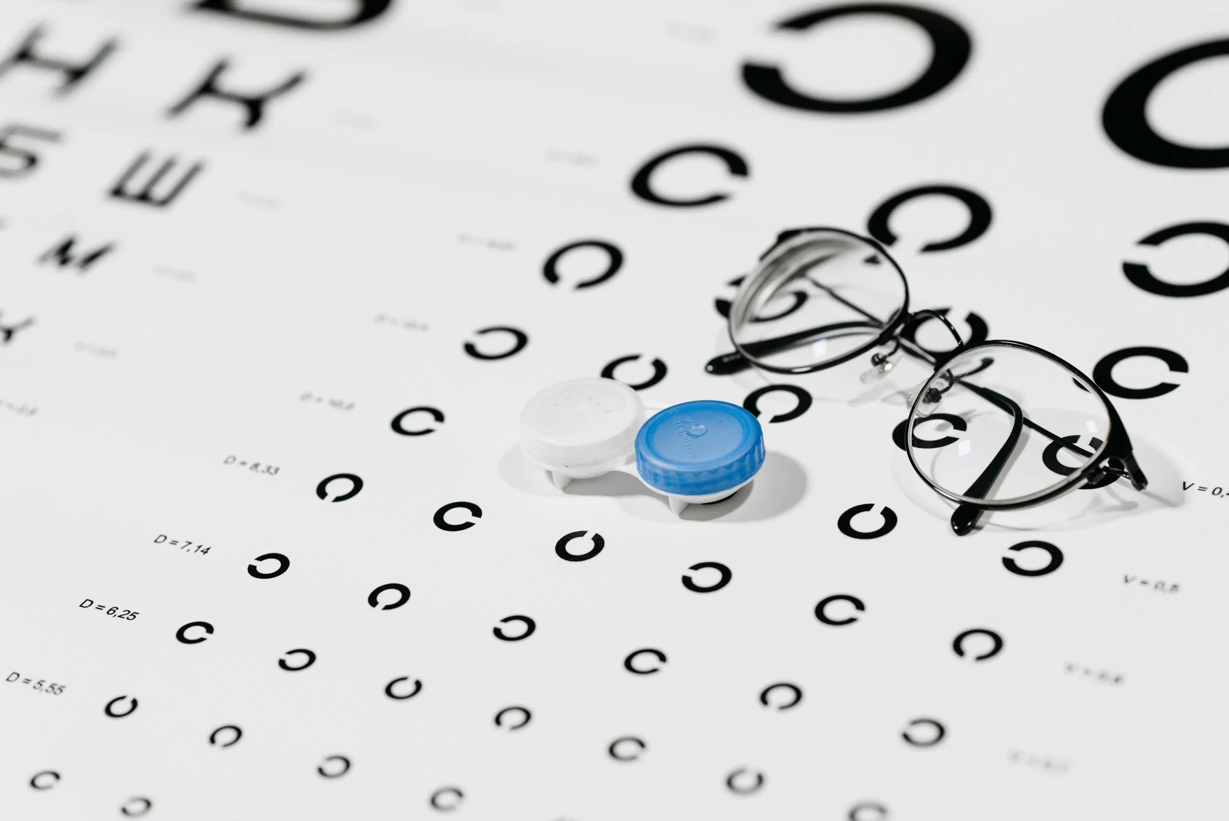 A pair of eyeglasses, eye drops bottles, and an eye chart with black letters on a white background.