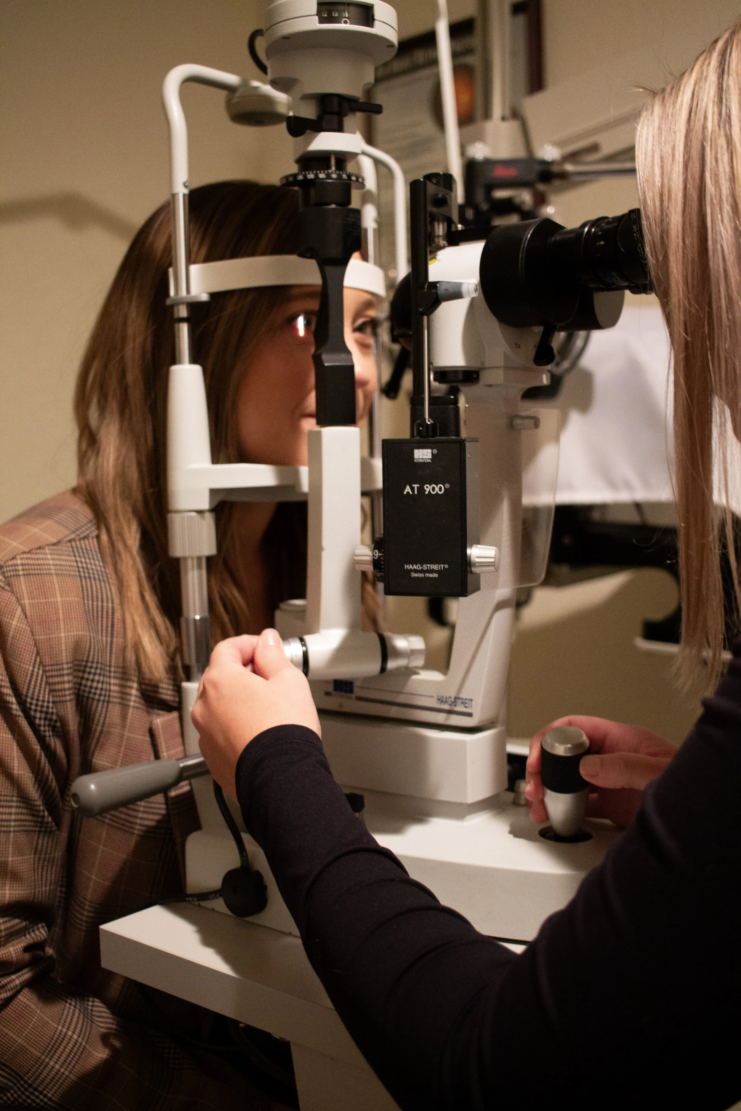 An optometrist is examining a patient's eyes using a slit lamp microscope in an eye clinic.
