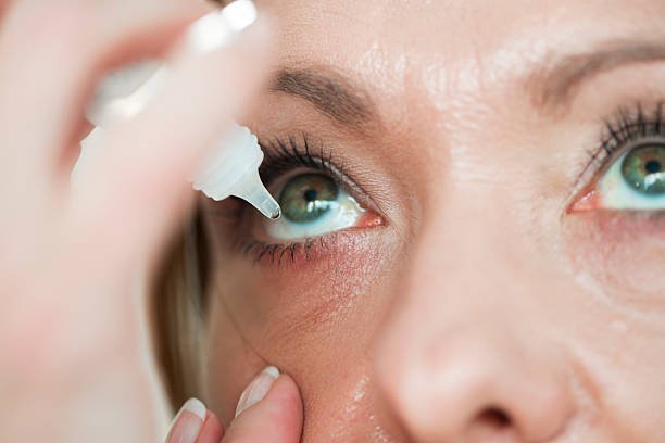 Close-up of a woman applying eye dropper to her eye.
