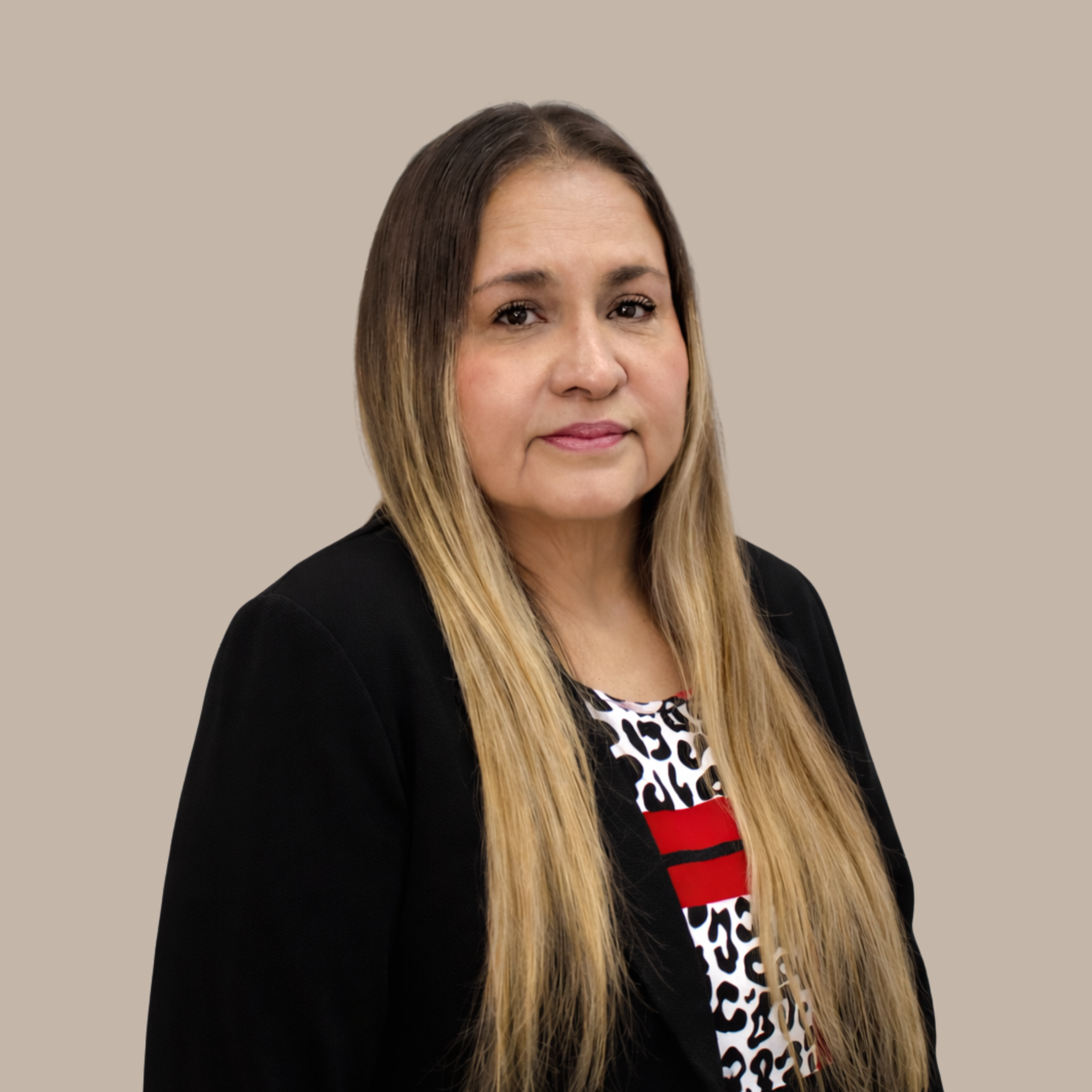 Professional woman with long blonde hair wearing a black blazer and a patterned top, neutral background.