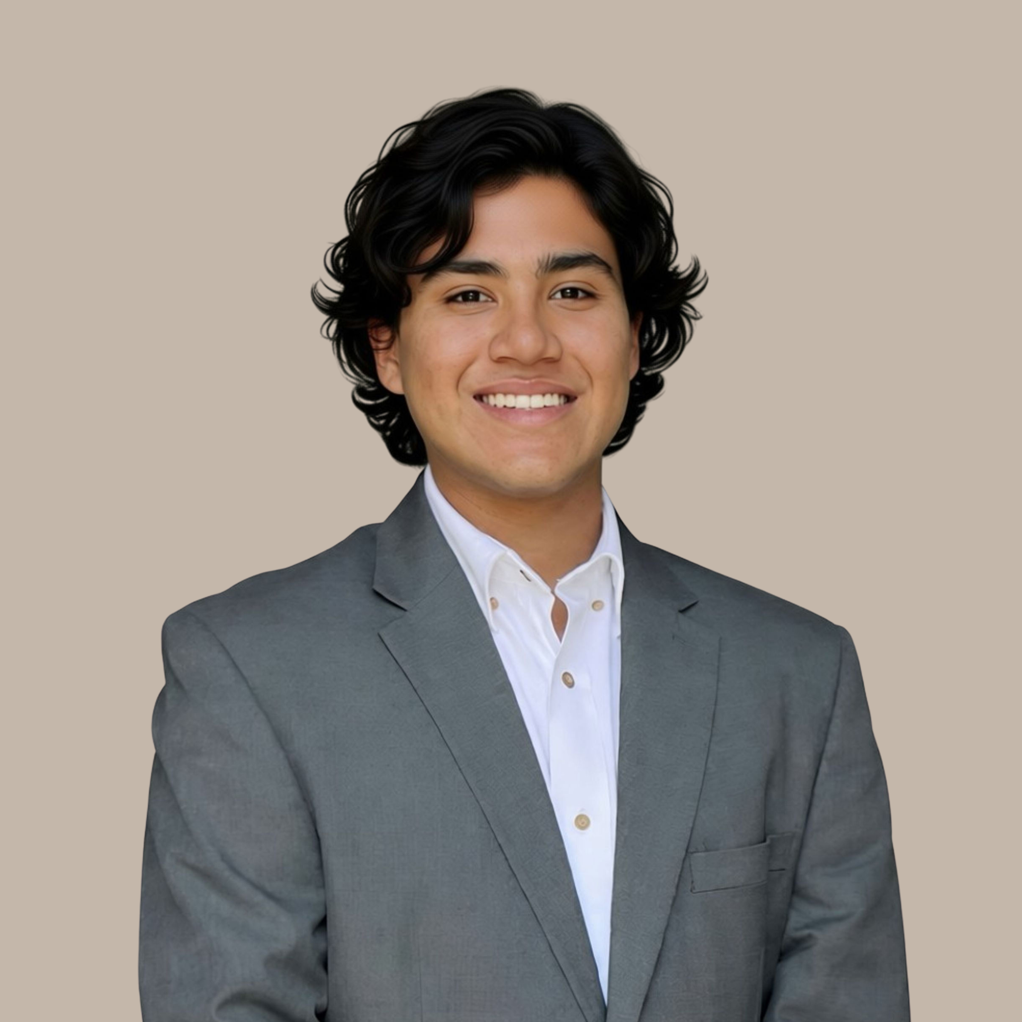 Young man with dark, wavy hair, wearing a gray suit and white shirt, smiling at the camera, beige background.