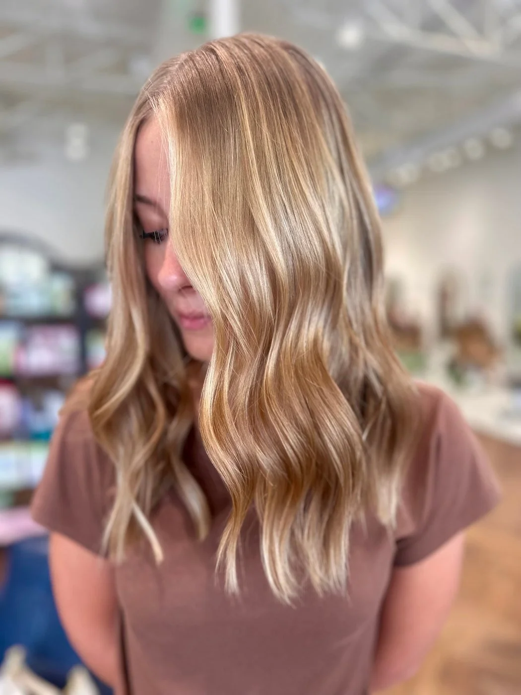 Woman looking down, with wavy honey-blonde balayage, a deeper root and brighter face-framing pieces