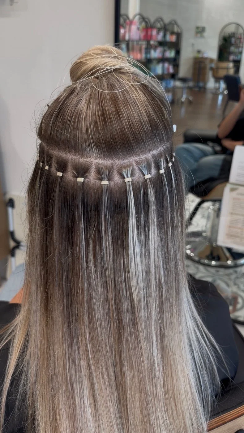 Back of a client's head with the top section pinned up and a row of beaded hair extensions attached underneath
