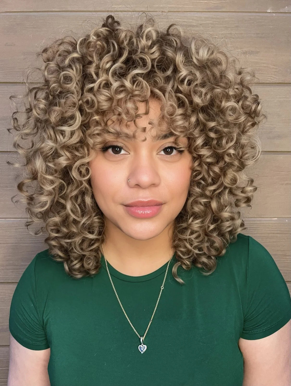 Woman with shoulder-length blonde curls and a curly fringe, wearing a green T-shirt