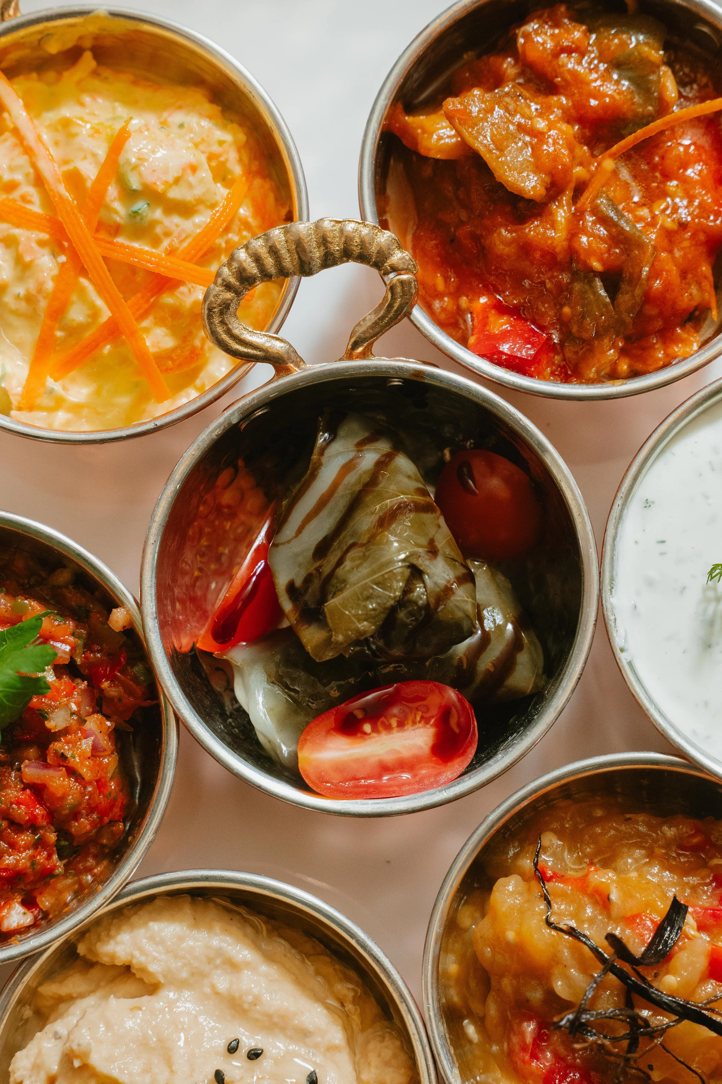 Assorted Indian condiments and dishes in small metal bowls, including chutneys, vegetable curries, and raita.