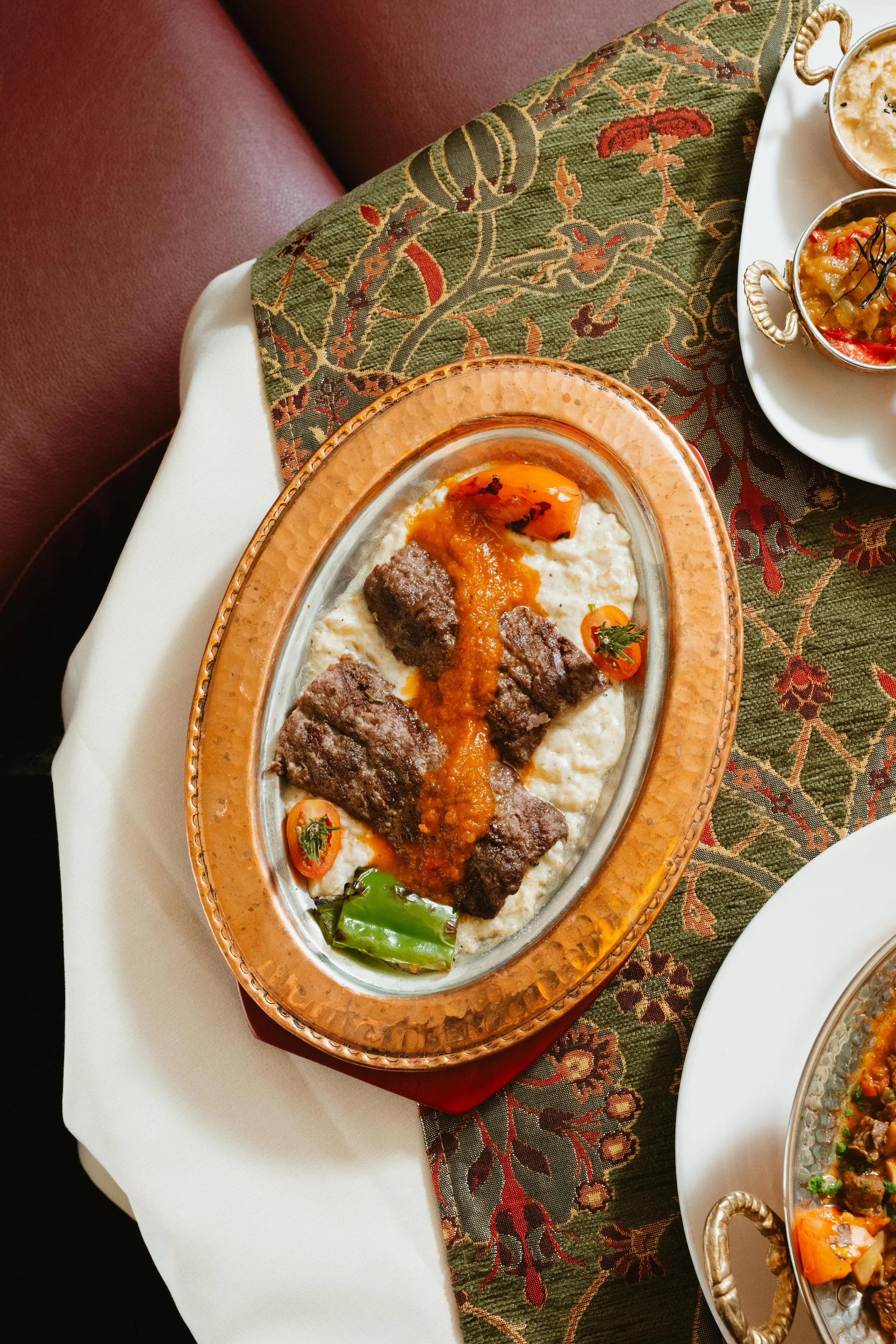 A plate of traditional Persian stew with grilled meat, tomato sauce, rice, and garnishes on an elegant dinner table.