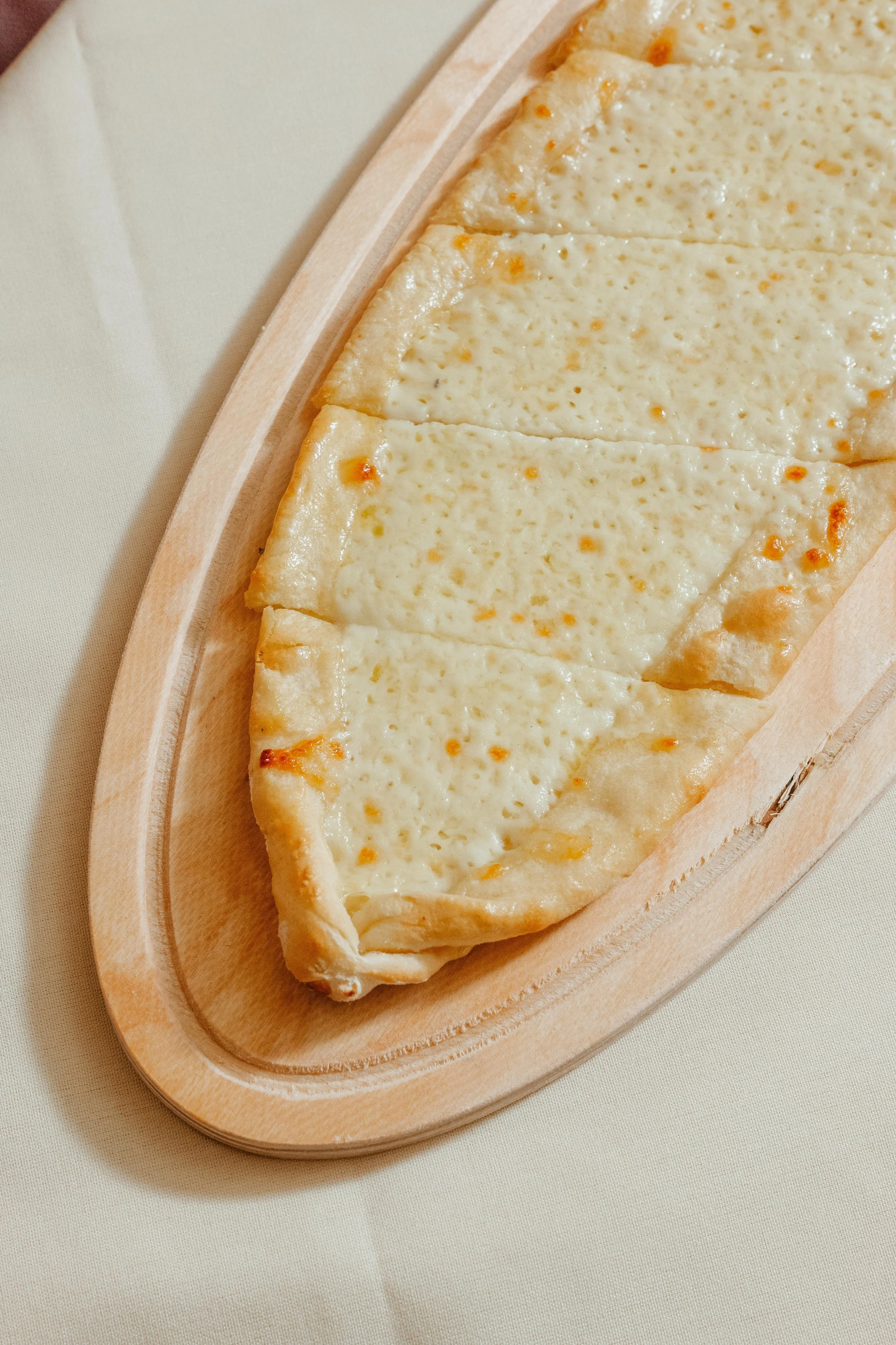 Cheese pizza sliced into pieces on a wooden serving tray.