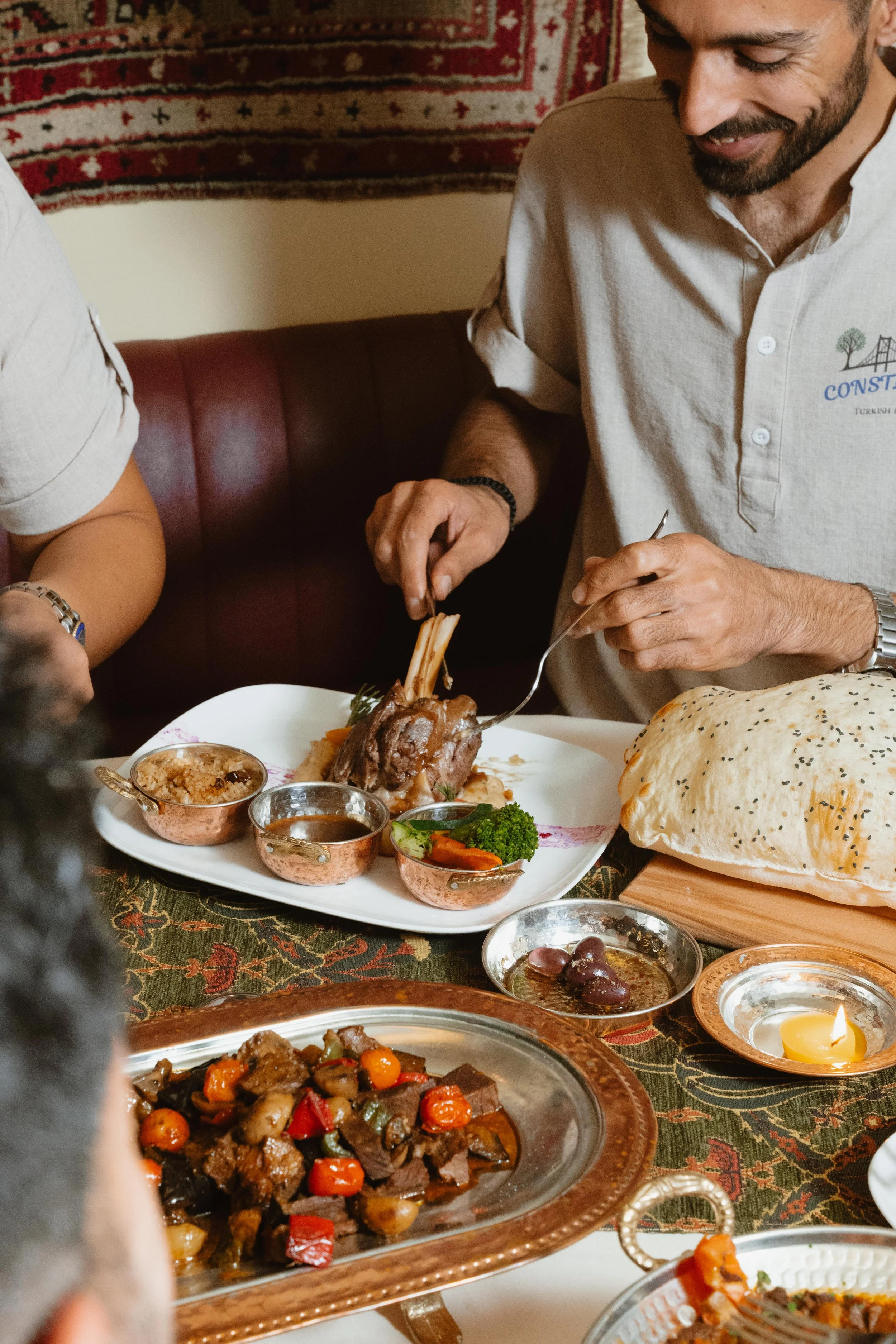 People enjoying a meal with Middle Eastern dishes, including lamb, vegetables, bread, and various side dishes on a table.