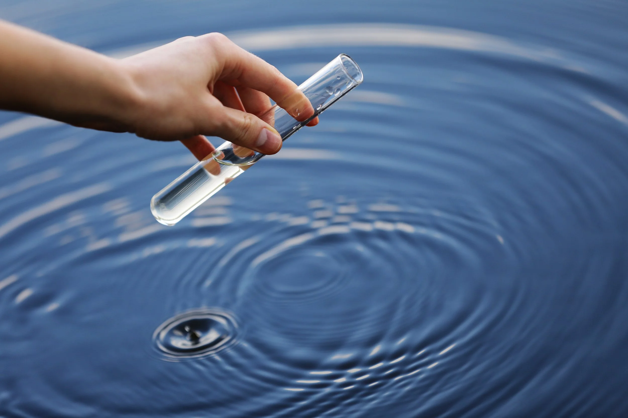 Hand holding a glass test tube filled with water, with ripples on the water's surface.