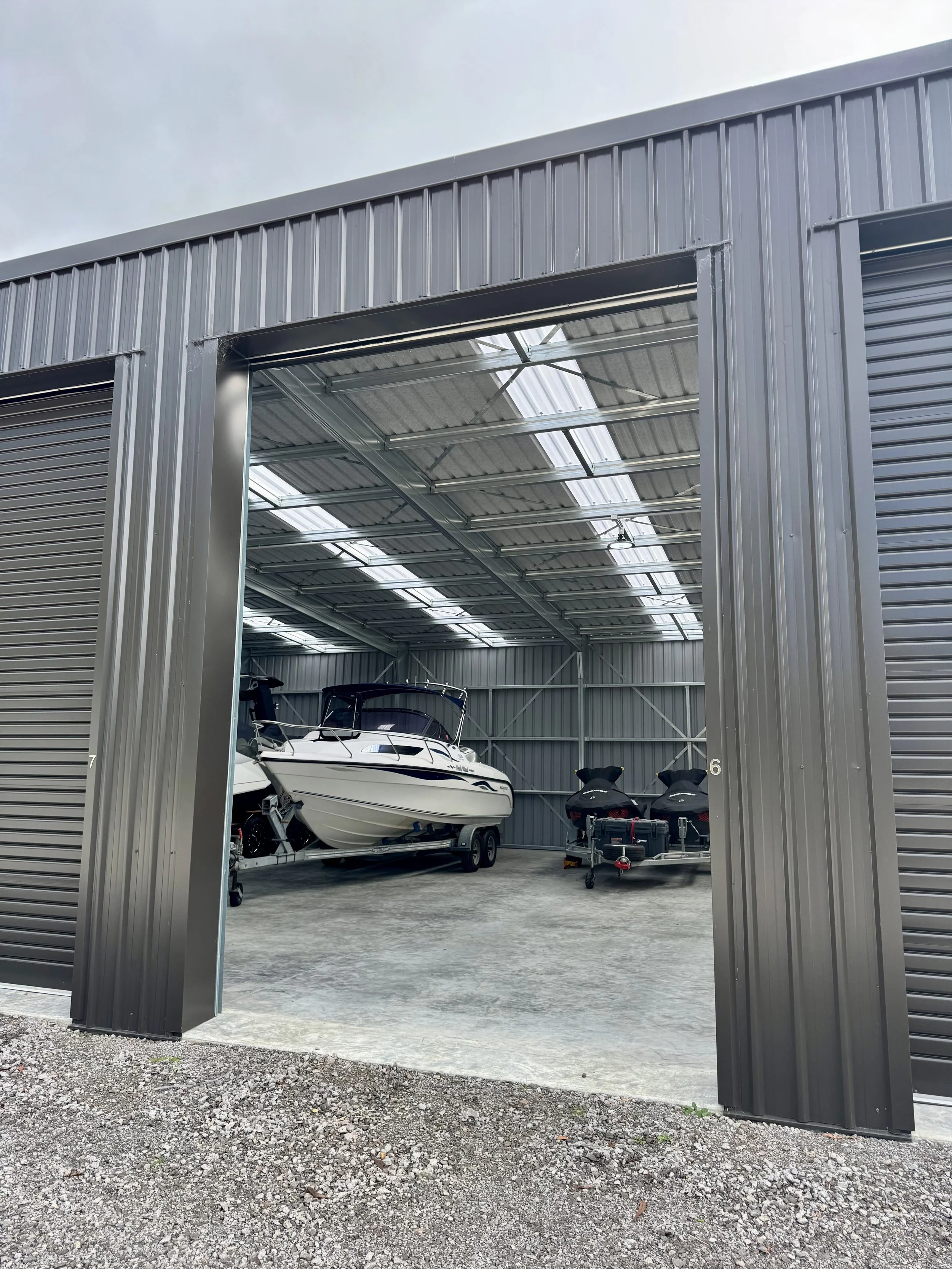 View of a metal boat storage building with an open door, showing two boats and two jet skis inside, with a concrete floor and metal roof.