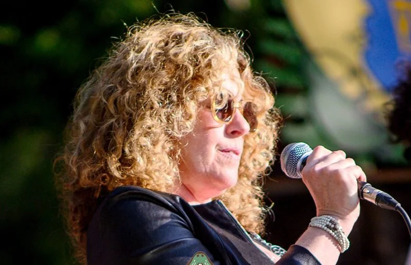 A singer with curly hair and sunglasses at the mic