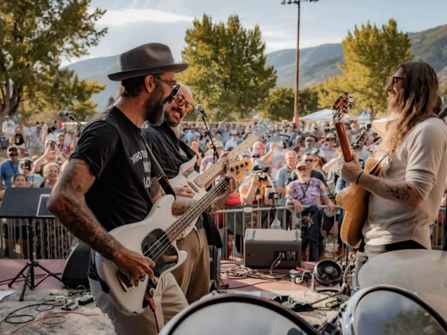Three players trading licks on stage with mountains behind