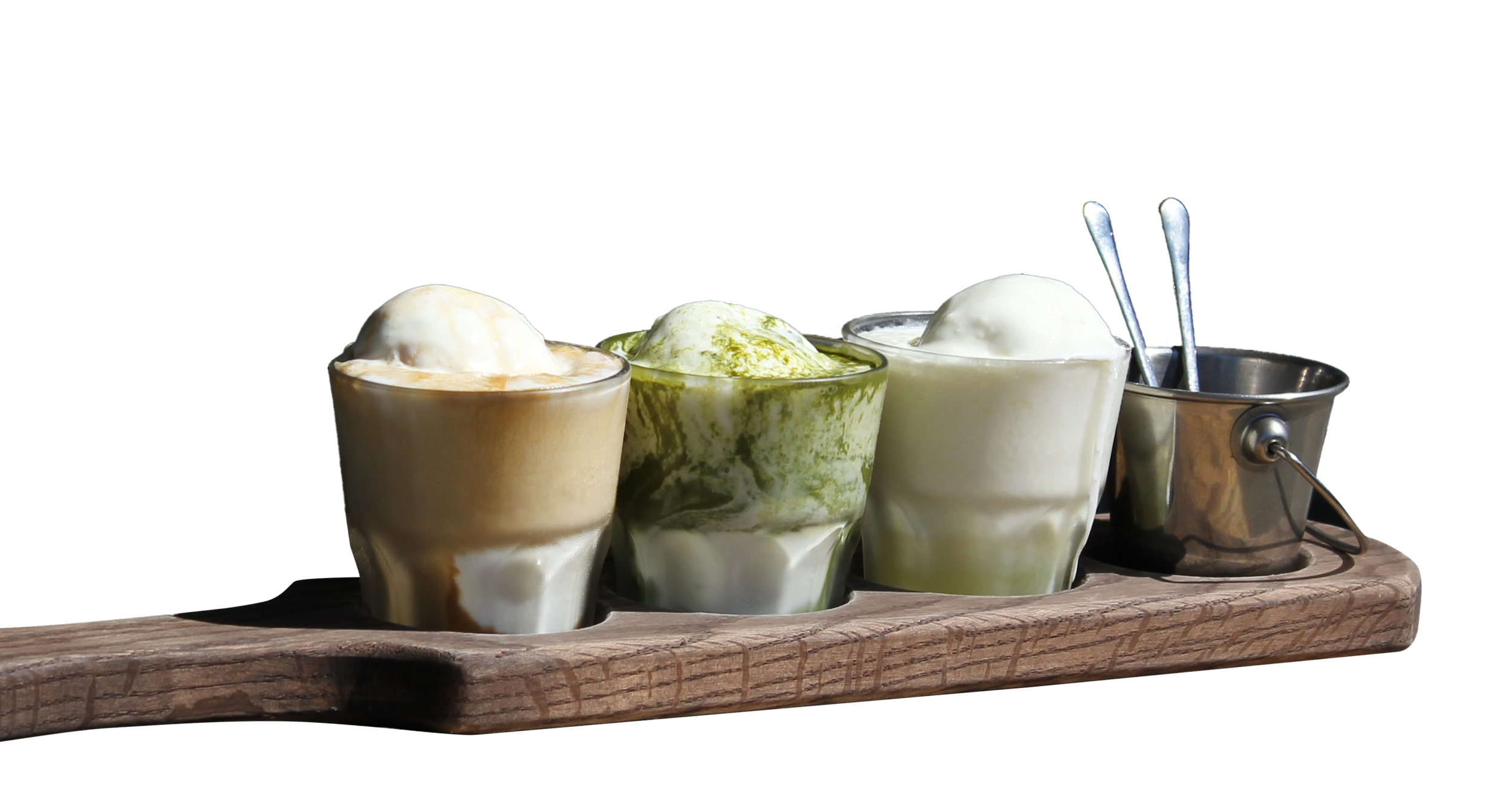 Three glasses of ice cream on a wooden board, each with a different flavor, with two metal spoons in a small metal container at the end.