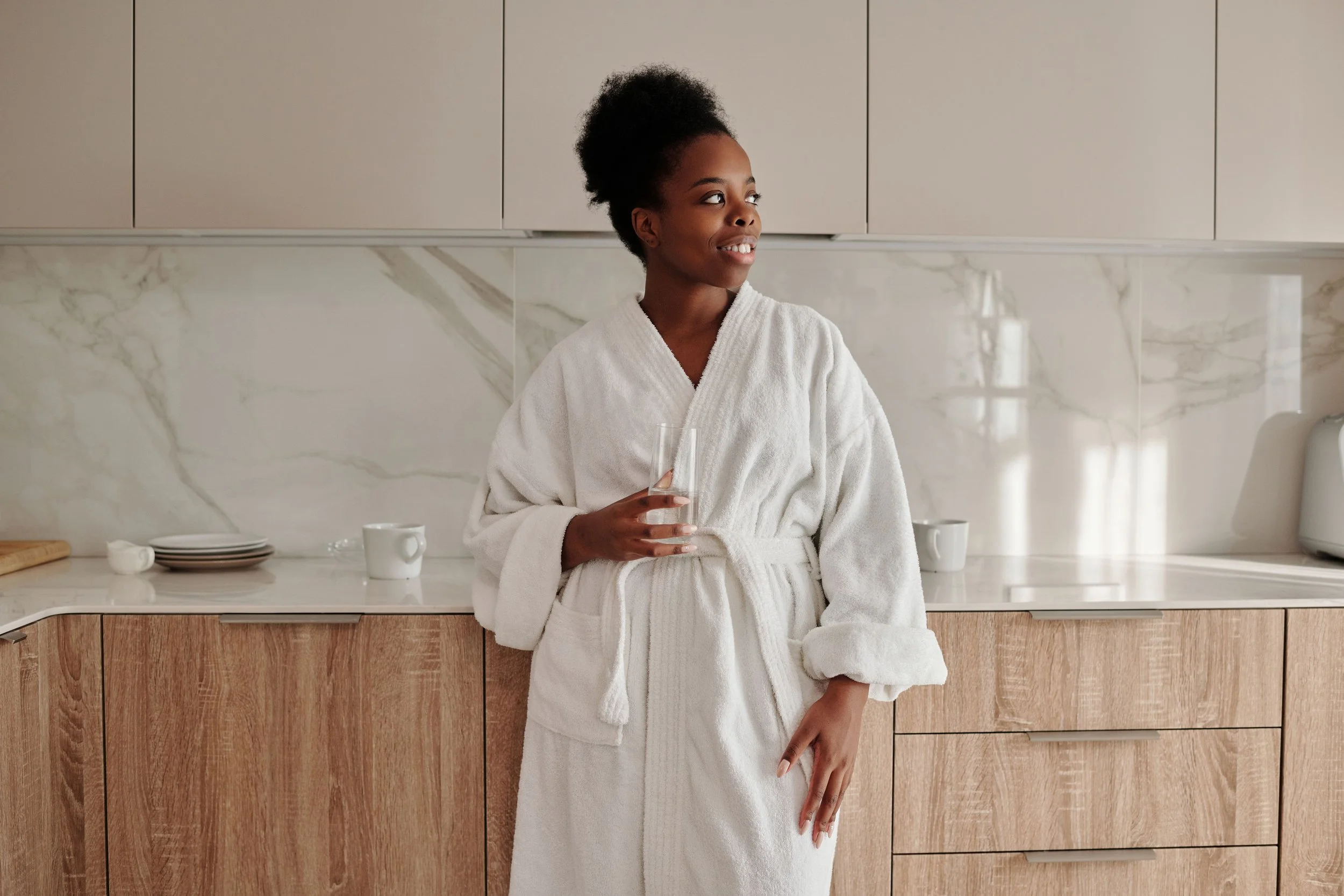 woman in white robe, holding glass of water, wellness | The Sectional