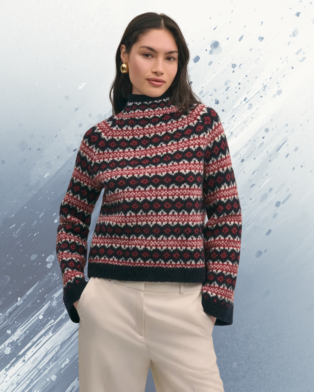 A woman wearing a patterned knit sweater with red, black, and white colors, and beige pants. She has dark hair, gold earrings, and stands against a light blue background with paint splatter effects.