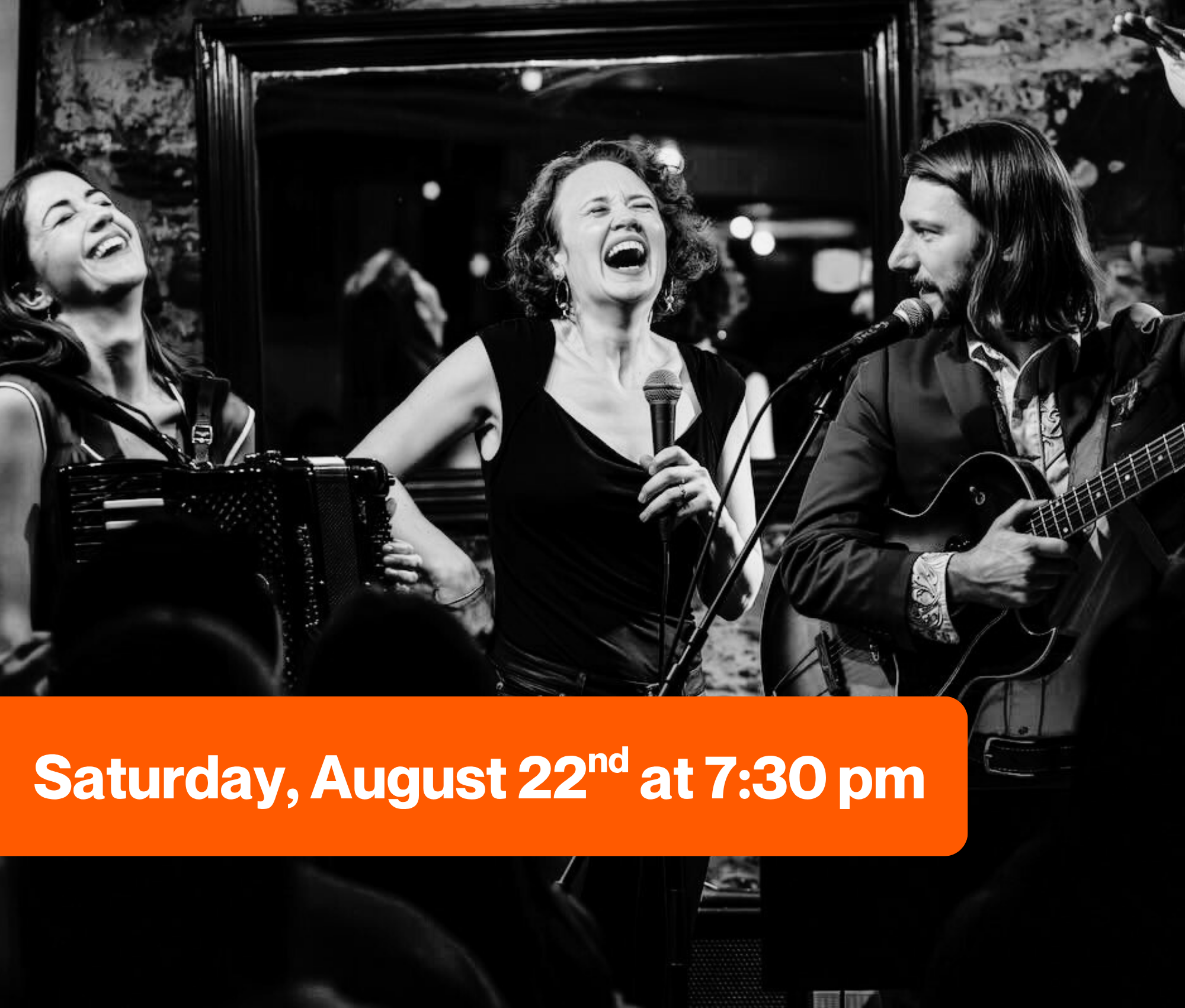 Three musicians performing on stage: a woman with an accordion on the left, a woman singing with a microphone in the center, and a man playing guitar on the right; all are enjoying the moment.