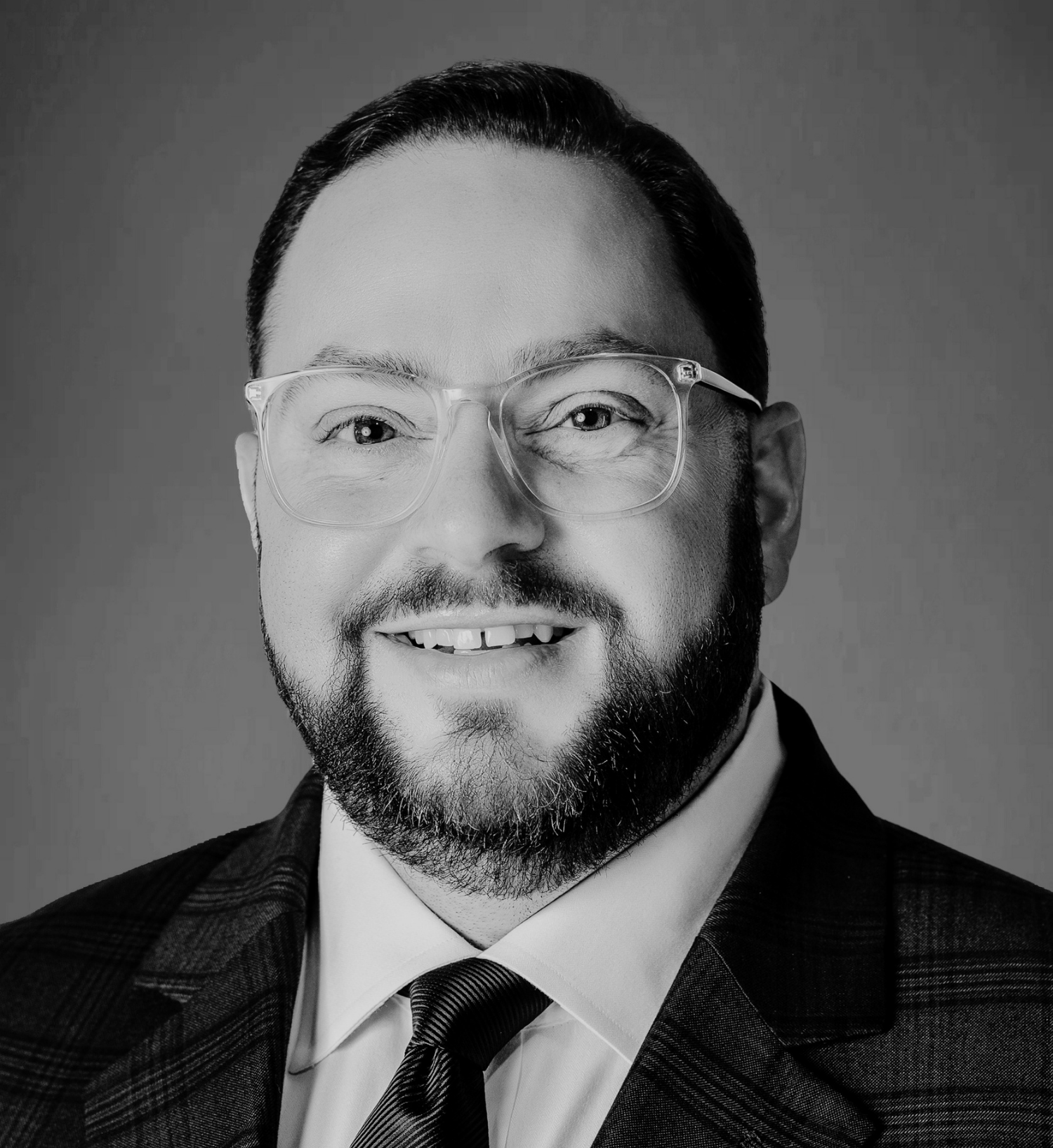 Black and white headshot of a man, David Whitehill, with glasses, a beard, and short hair, wearing a suit and tie, smiling.