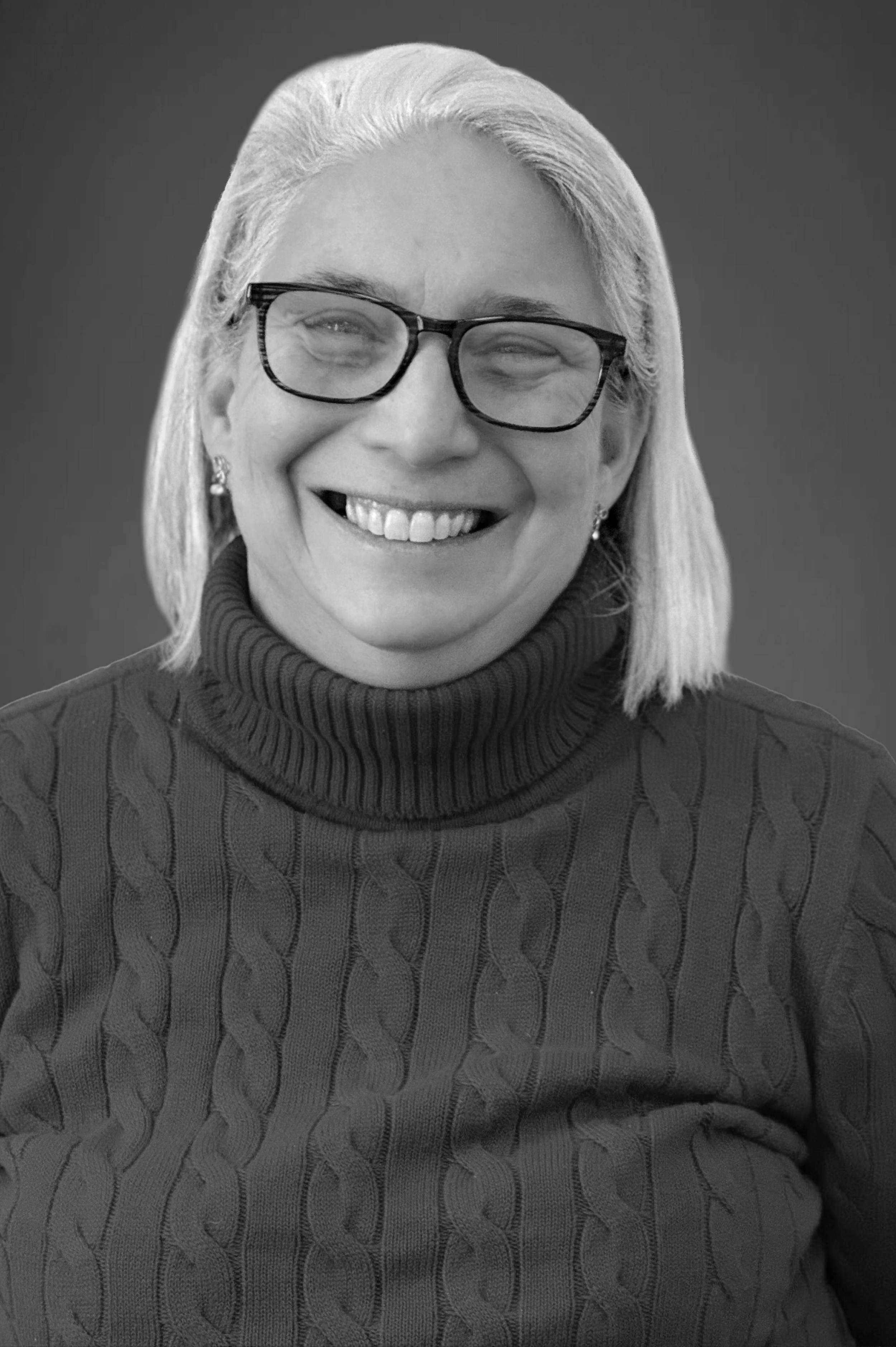 A smiling woman, Robin Pomeranz, with glasses and earrings wearing a cable-knit turtleneck sweater.