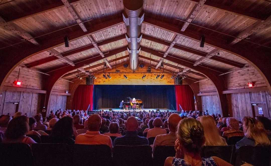 People watching a musical concert on stage in a rustic wooden theater with an arched ceiling.