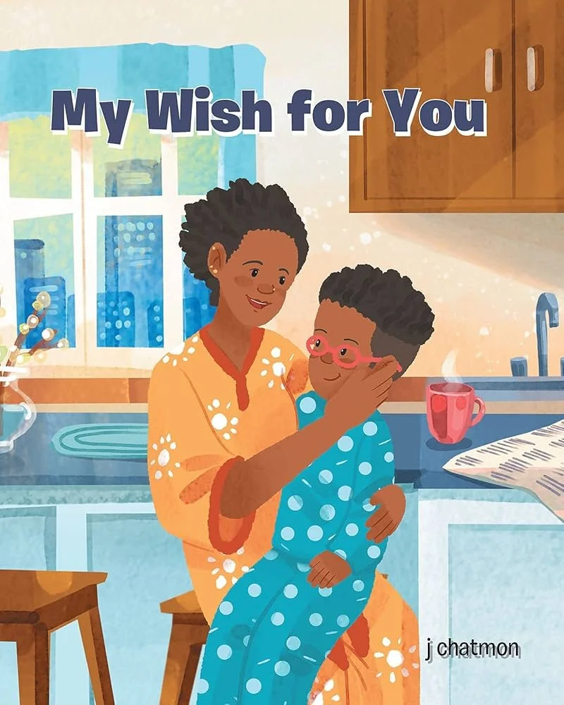 An illustration of a woman with short, curly hair and a young boy with glasses hugging in a kitchen. The woman is wearing an orange dress with white flowers, and the boy is in blue pajamas with white polka dots. There is a window, a red mug, a newspaper, and wooden cabinets in the background, with the words "My Wish for You" at the top.