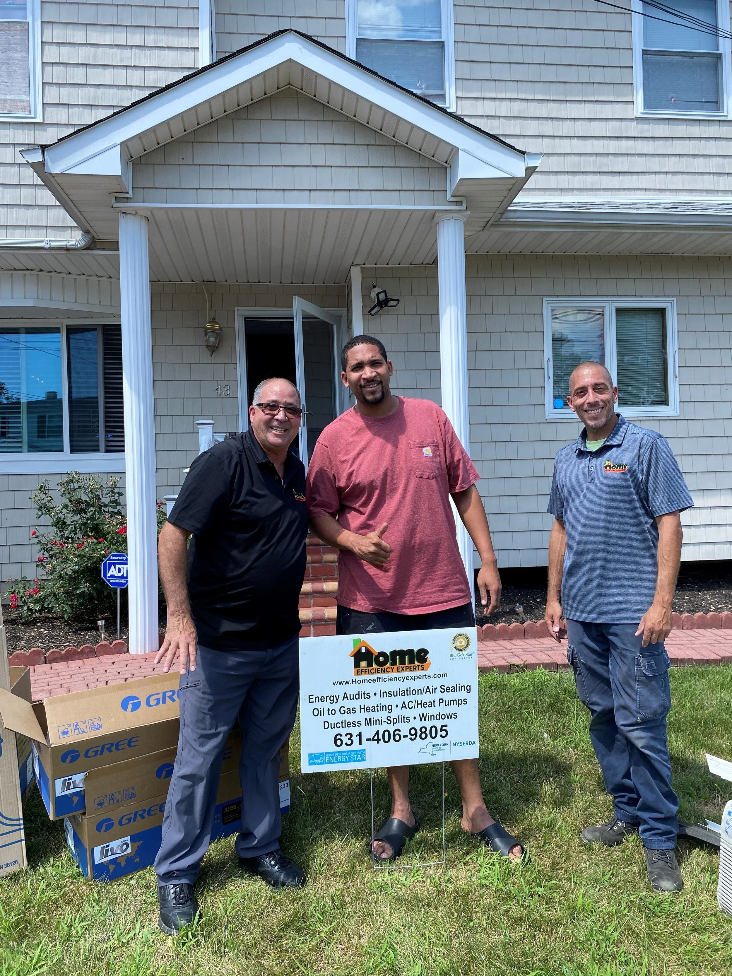 Three men standing in front of a house, smiling standing next to a sign for Home Efficiency Experts.