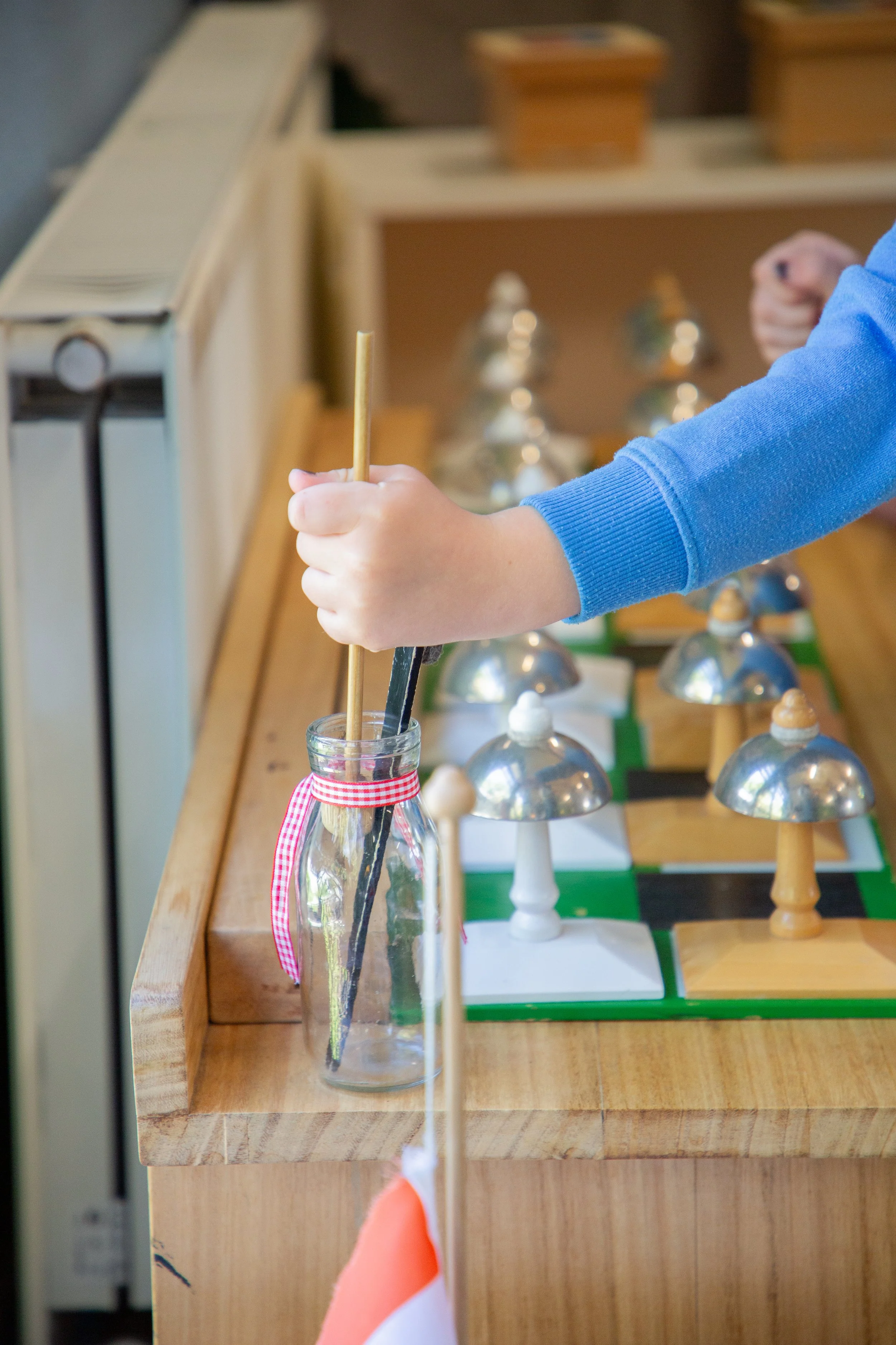 Child's hand placing a black chess piece into a glass jar on a wooden chess table.