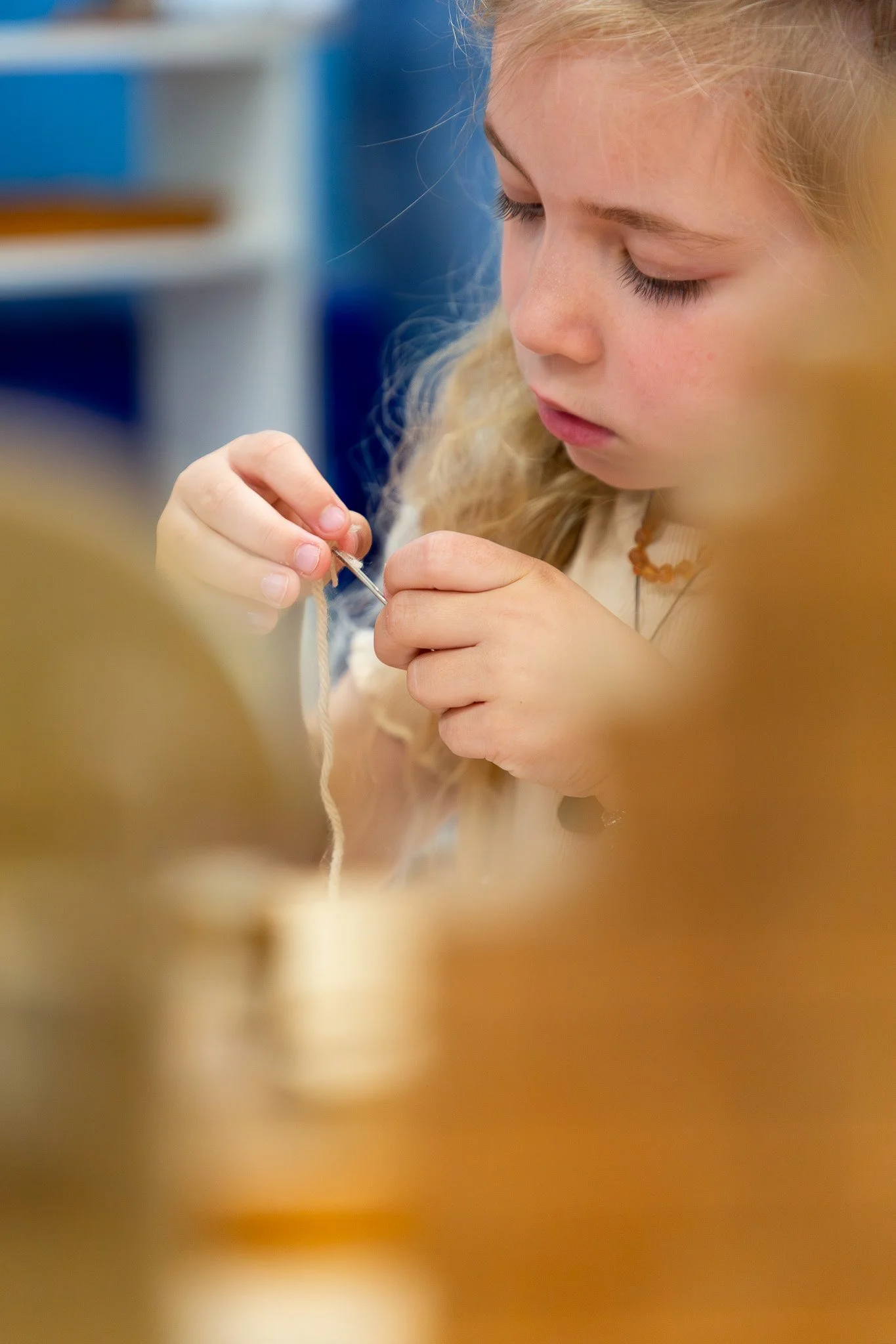 A young girl with blonde hair concentrating on a sewing project, using a needle and thread.