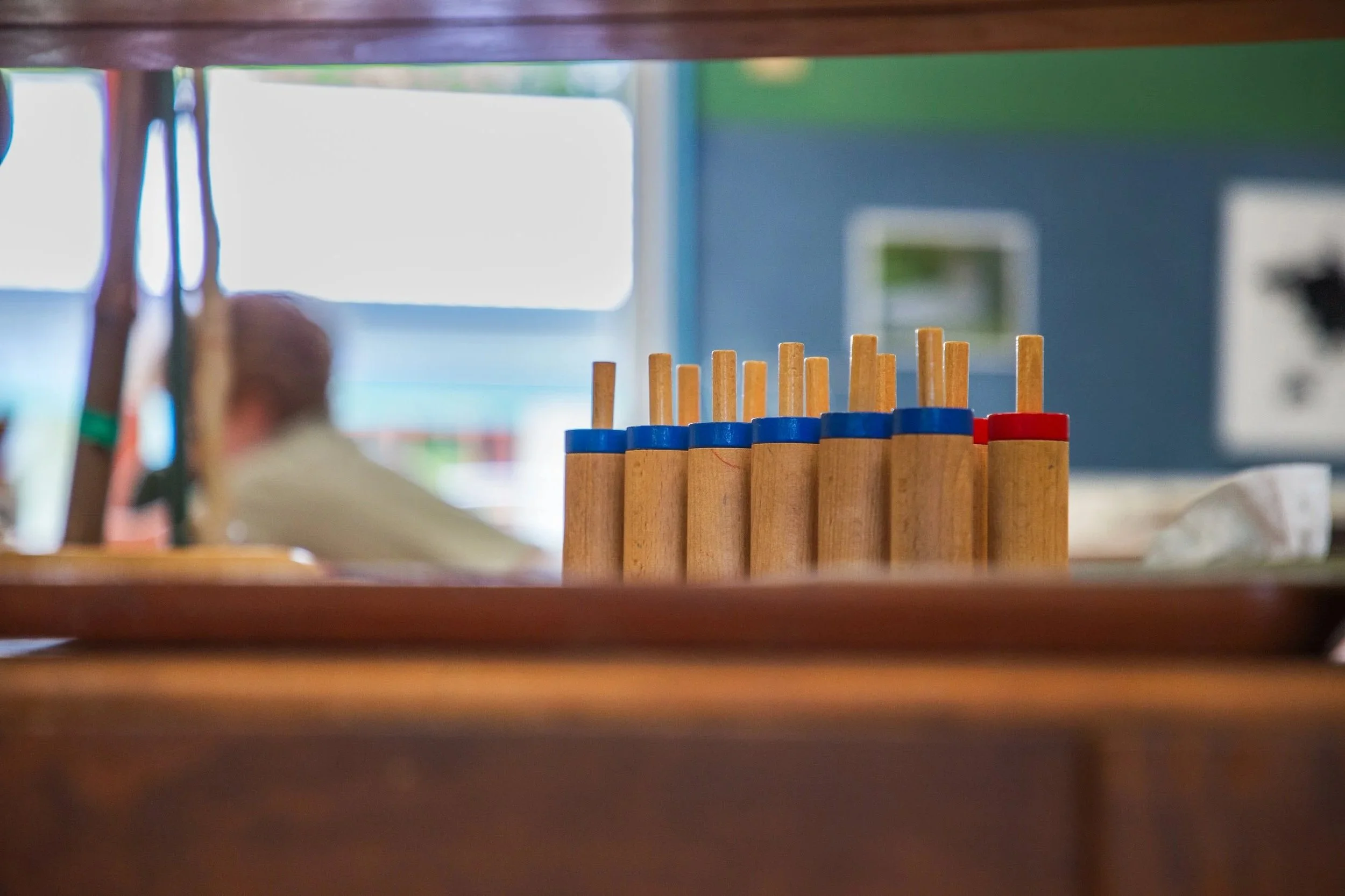 Close-up of wooden game pieces with colored rings placed on a table, with a blurred background of indoor setting and a person sitting.