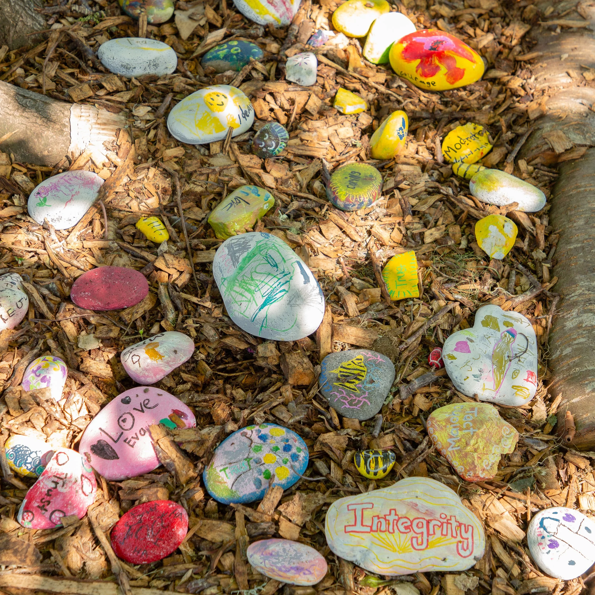 Painted rocks on ground with words and drawings, including 'Love' and 'Integrity'.