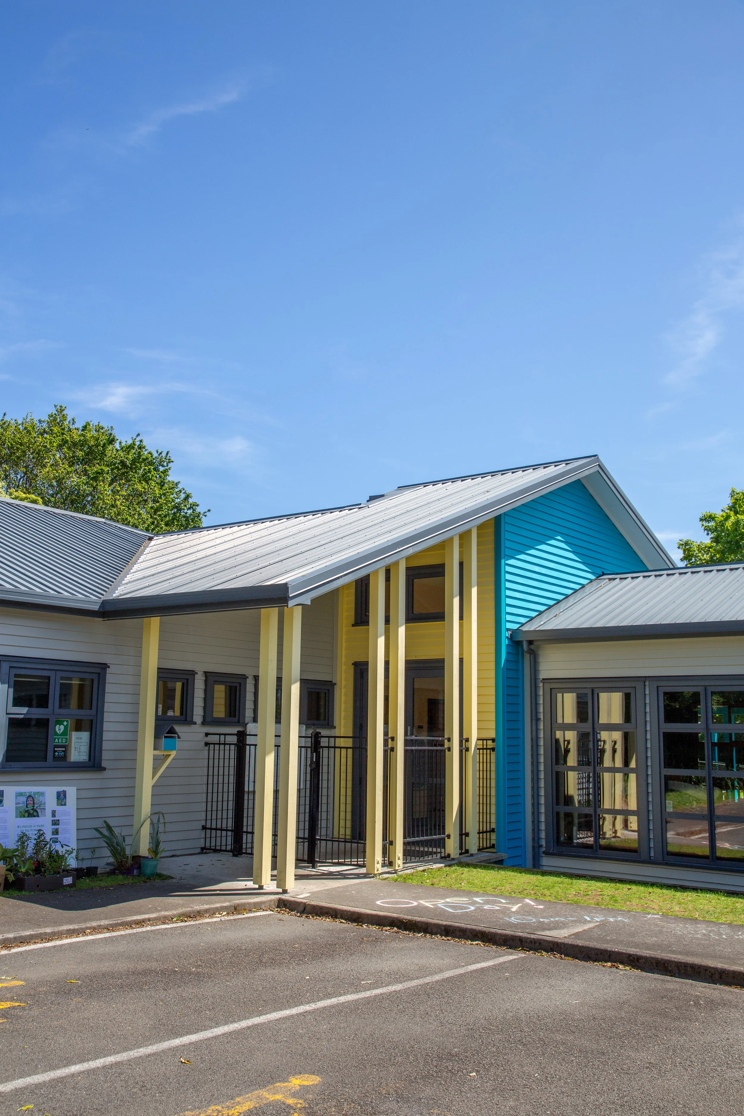 Colorful modern building with yellow and blue exterior, metal roof, large windows, and a small outdoor parking area with bike parking.