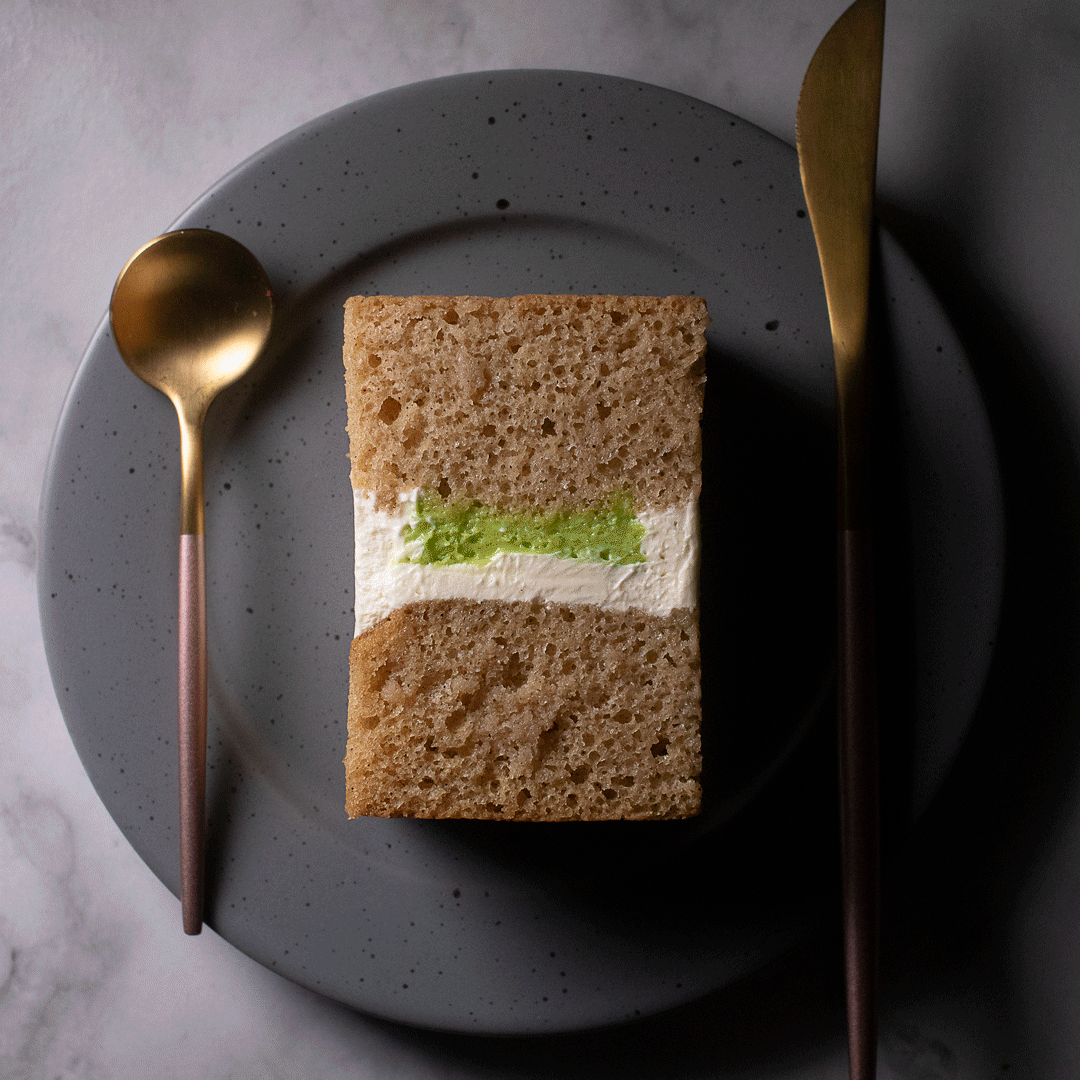 A plated dessert featuring a soft sponge cake with a buttercream and lemon pie filling, served with a gold spoon and fork on a gray speckled ceramic plate.