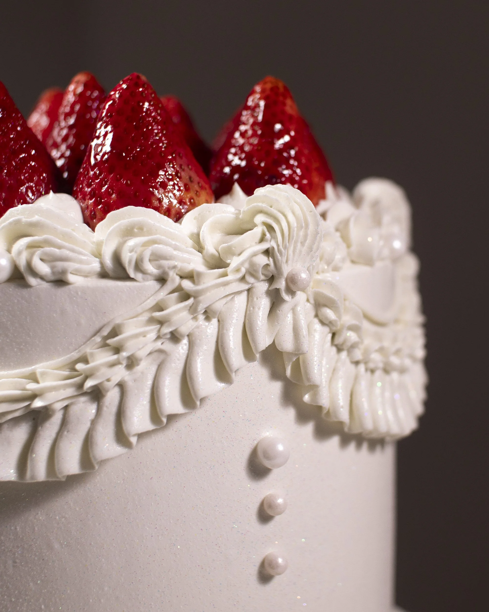 Close-up of a decorated cake with strawberries on top, white icing, and pearl-like decorations.
