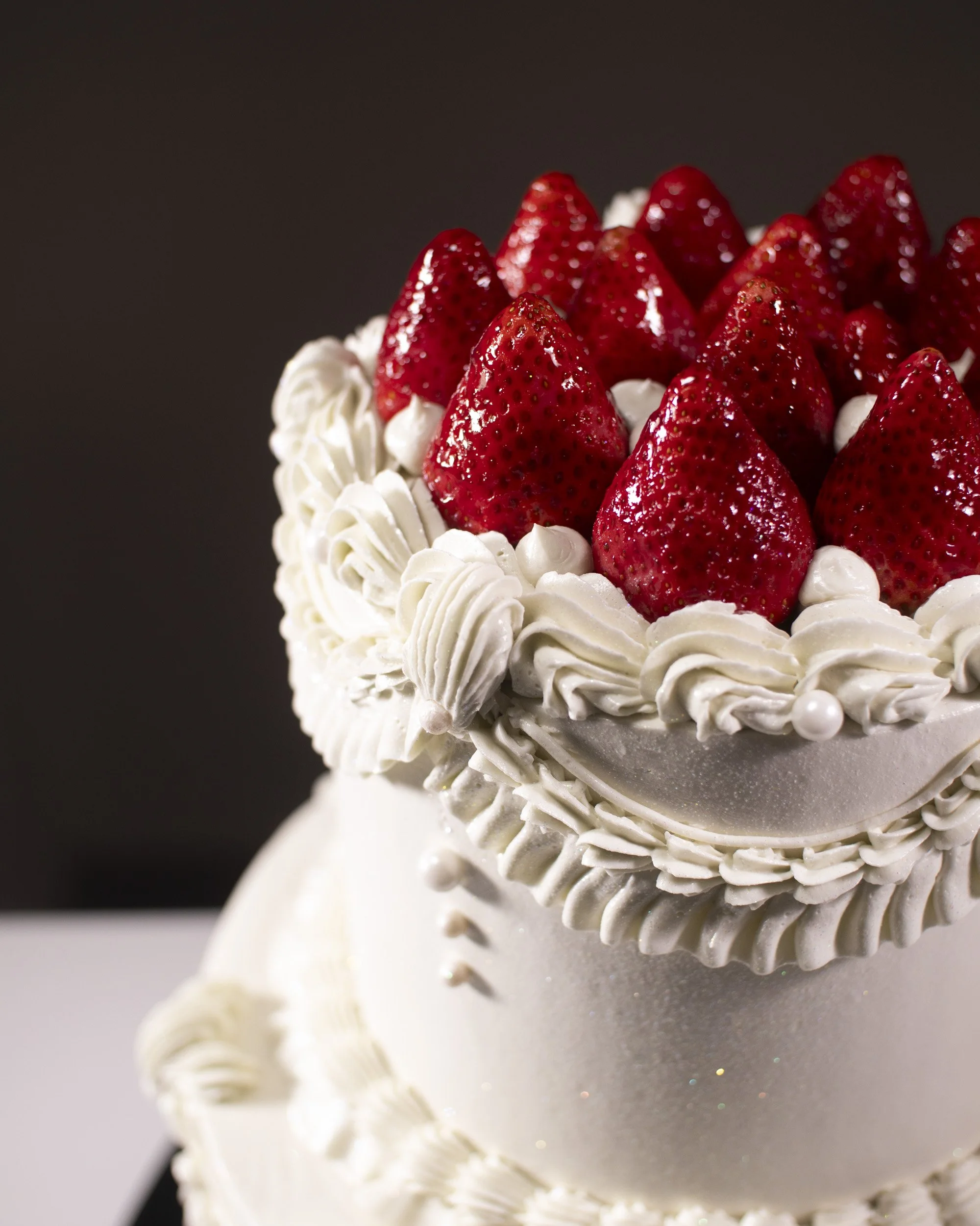 Close-up of a white cake decorated with whipped cream and topped with fresh strawberries.