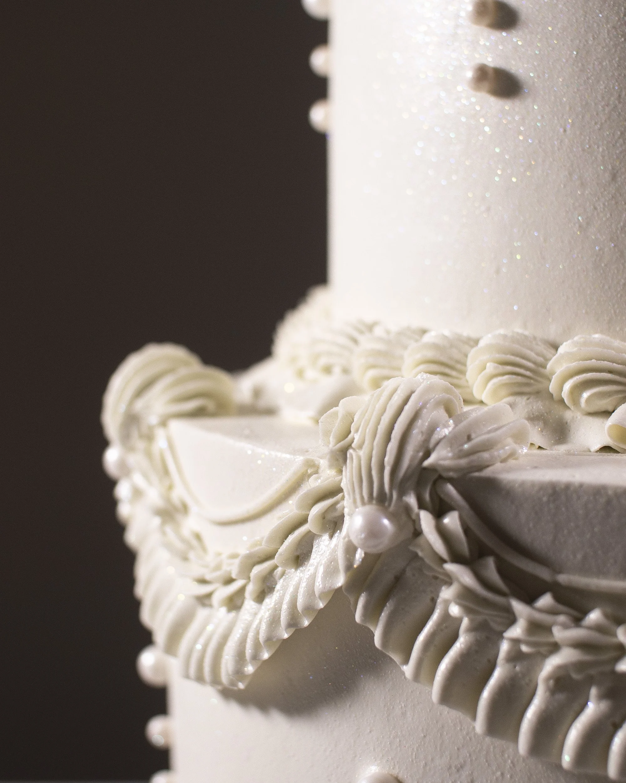 Close-up of a white wedding cake with piped icing decorations and pearl accents.