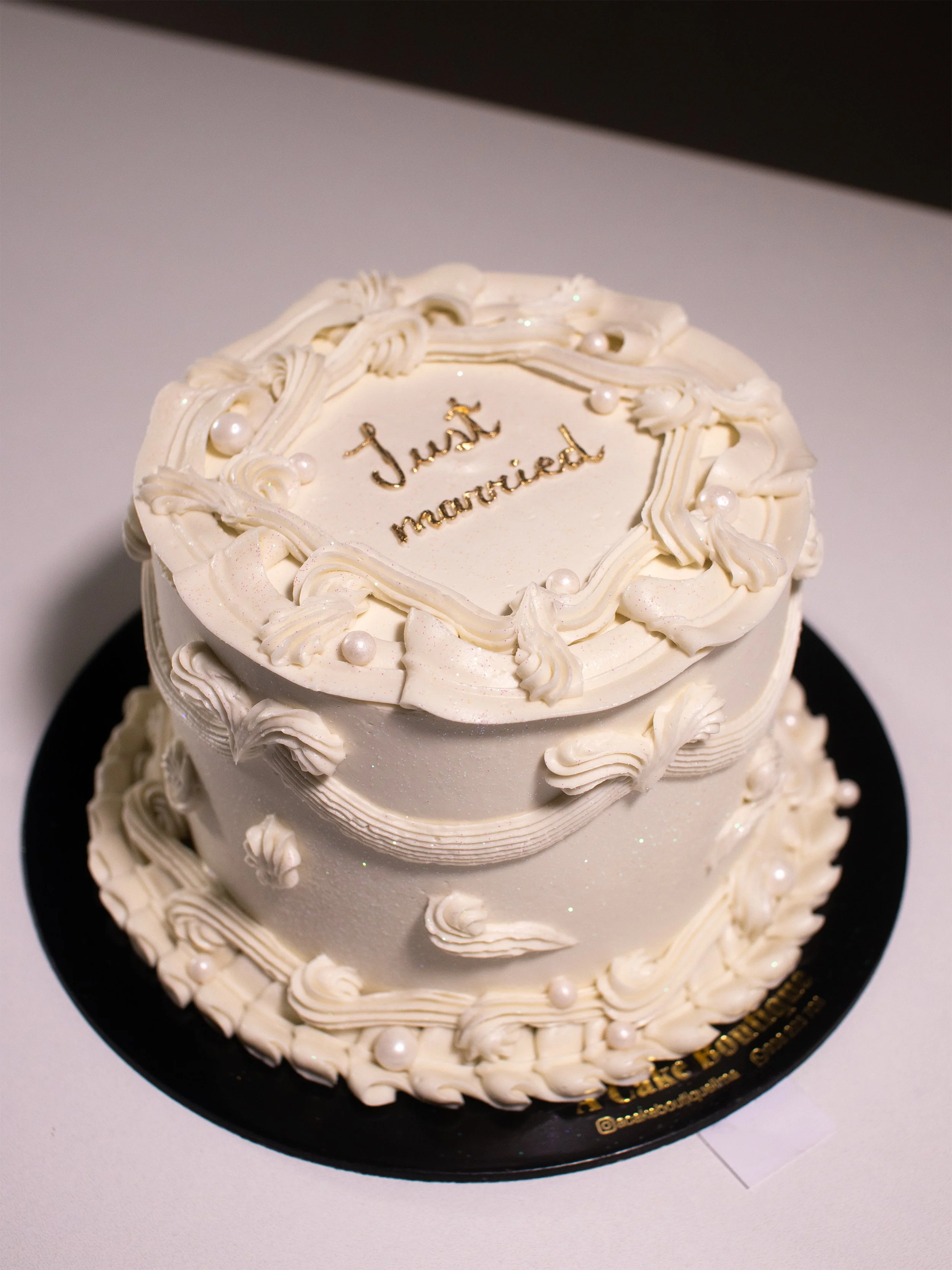 White wedding cake with piped icing decorations and pearls, with "Just Married" written on top.