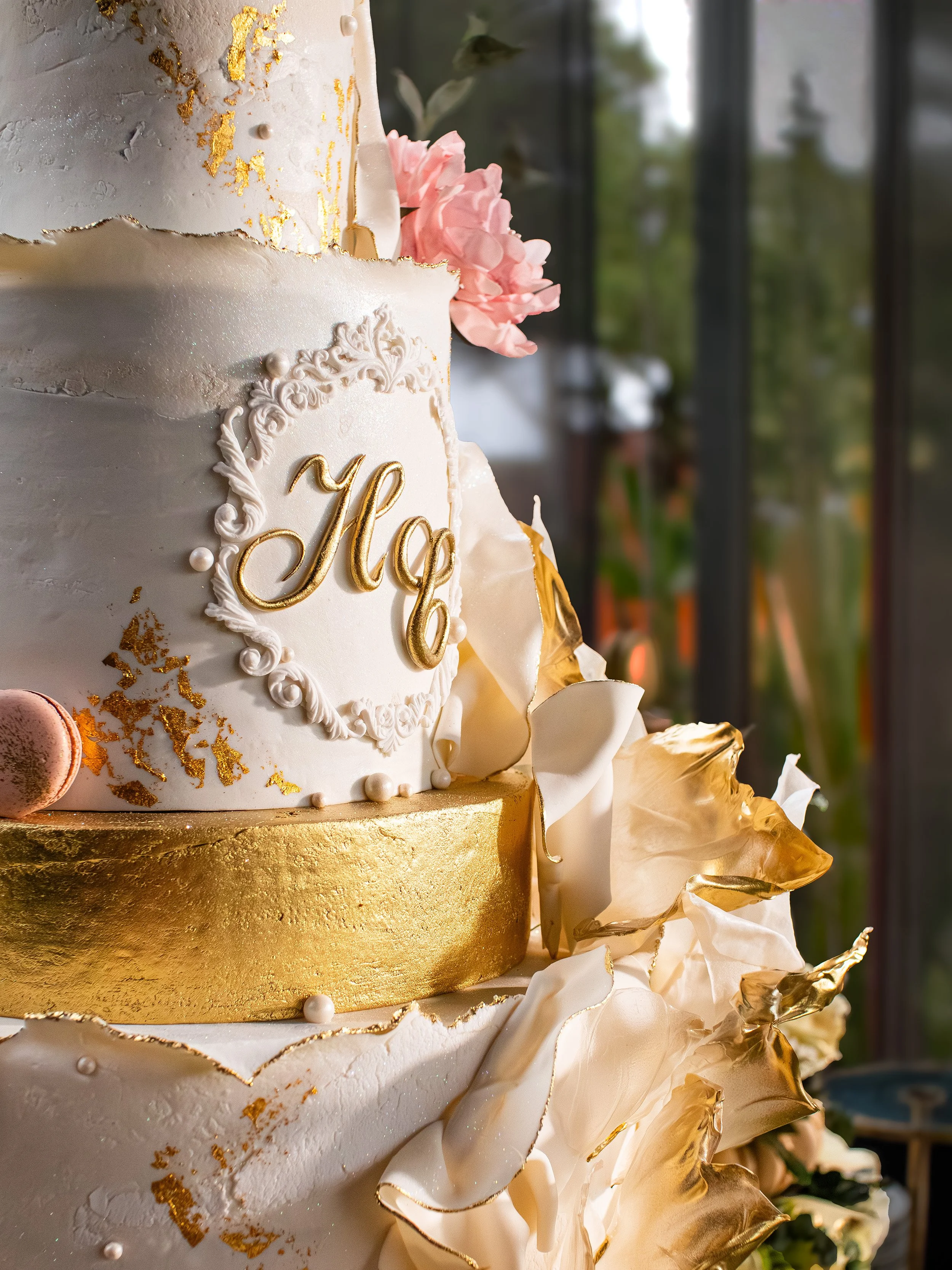 Close-up of a multi-tiered wedding cake decorated with white and gold elements, pink flowers, and ornate gold accents.