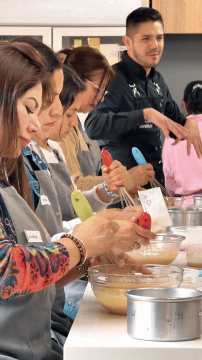 A group of people participating in a cooking class, mixing batter with colorful spatulas in a kitchen setting.