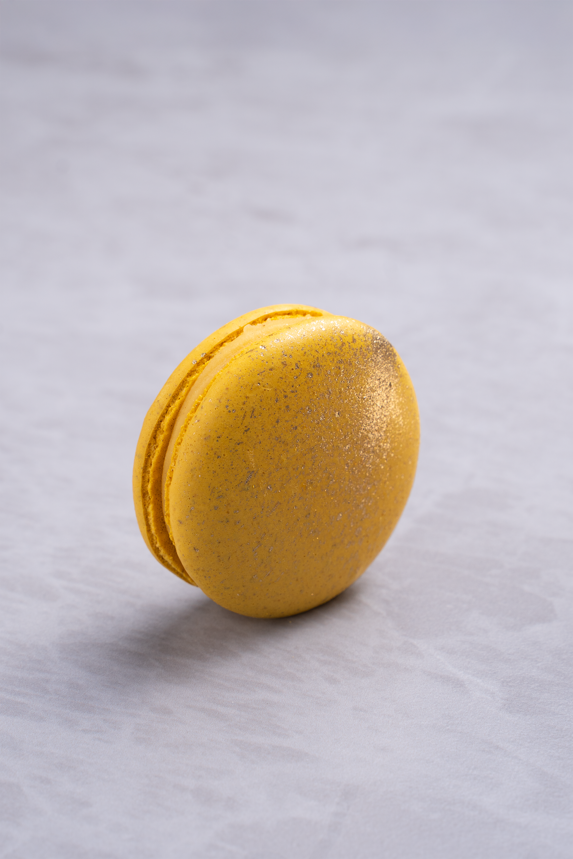 A yellow macaron with silver glitter on a light gray surface.