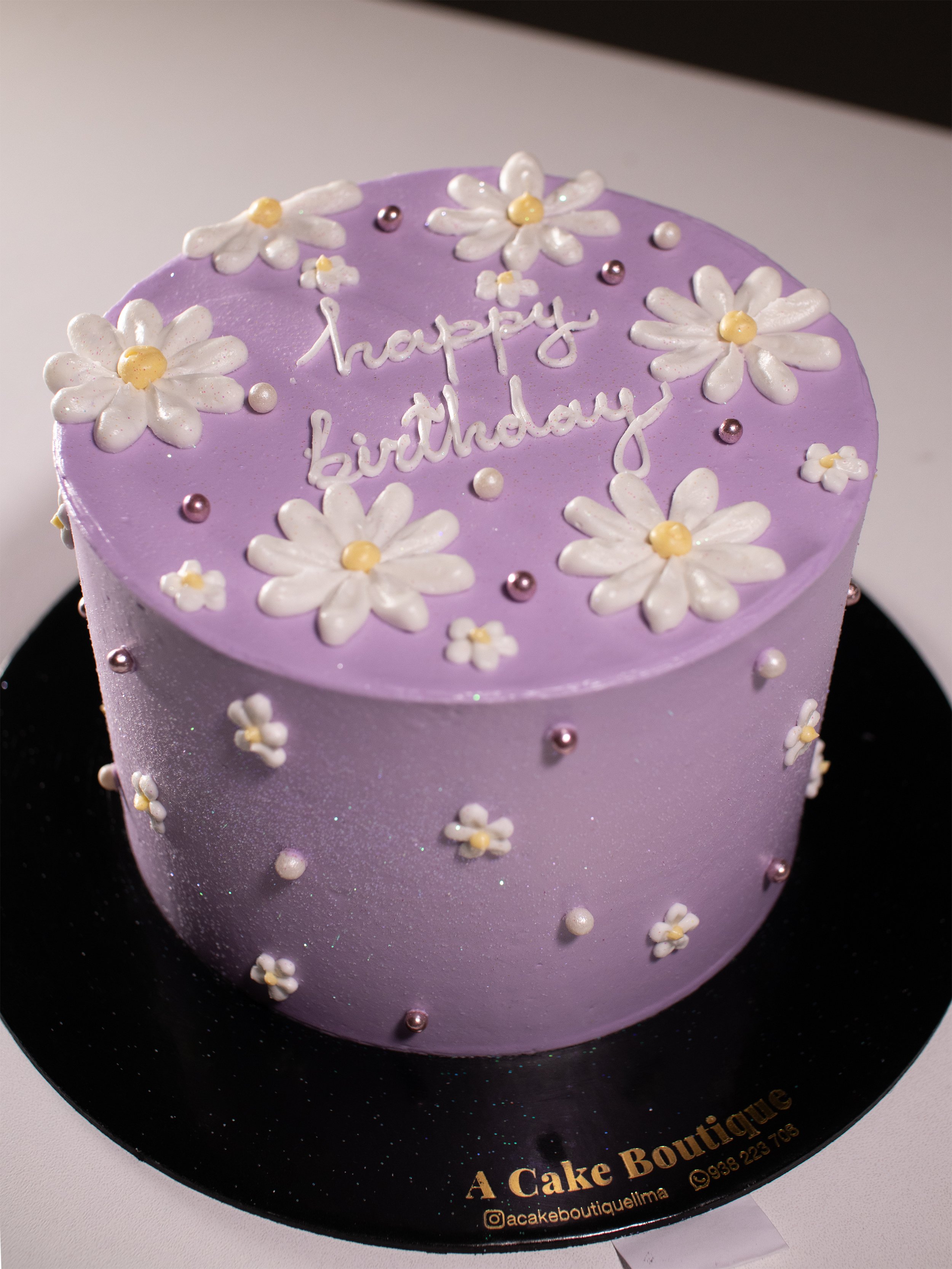 Purple birthday cake decorated with white flowers and small purple and white beads, with the words 'happy birthday' written on top.