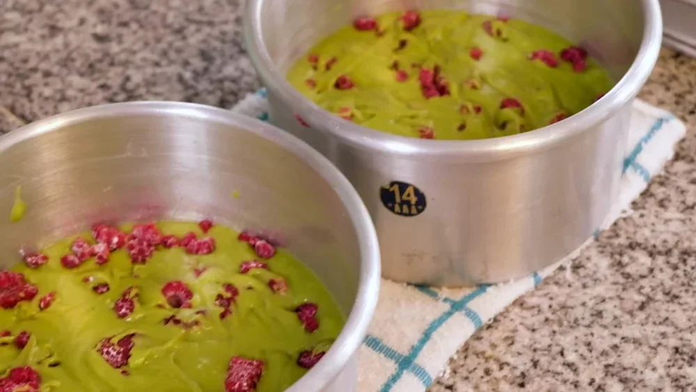 Two silver baking pans filled with a yellow-green mixture topped with small red fruit, placed on a kitchen countertop.