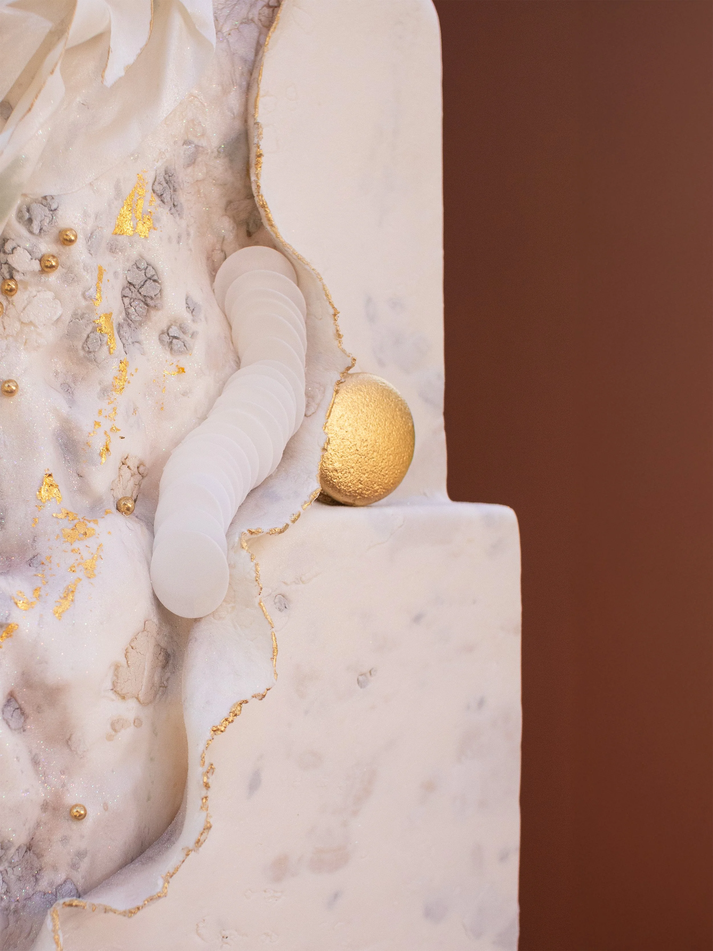 Close-up of a decorative cake with white and gold accents, featuring a gold spherical ornament and a row of white circular decorative elements.