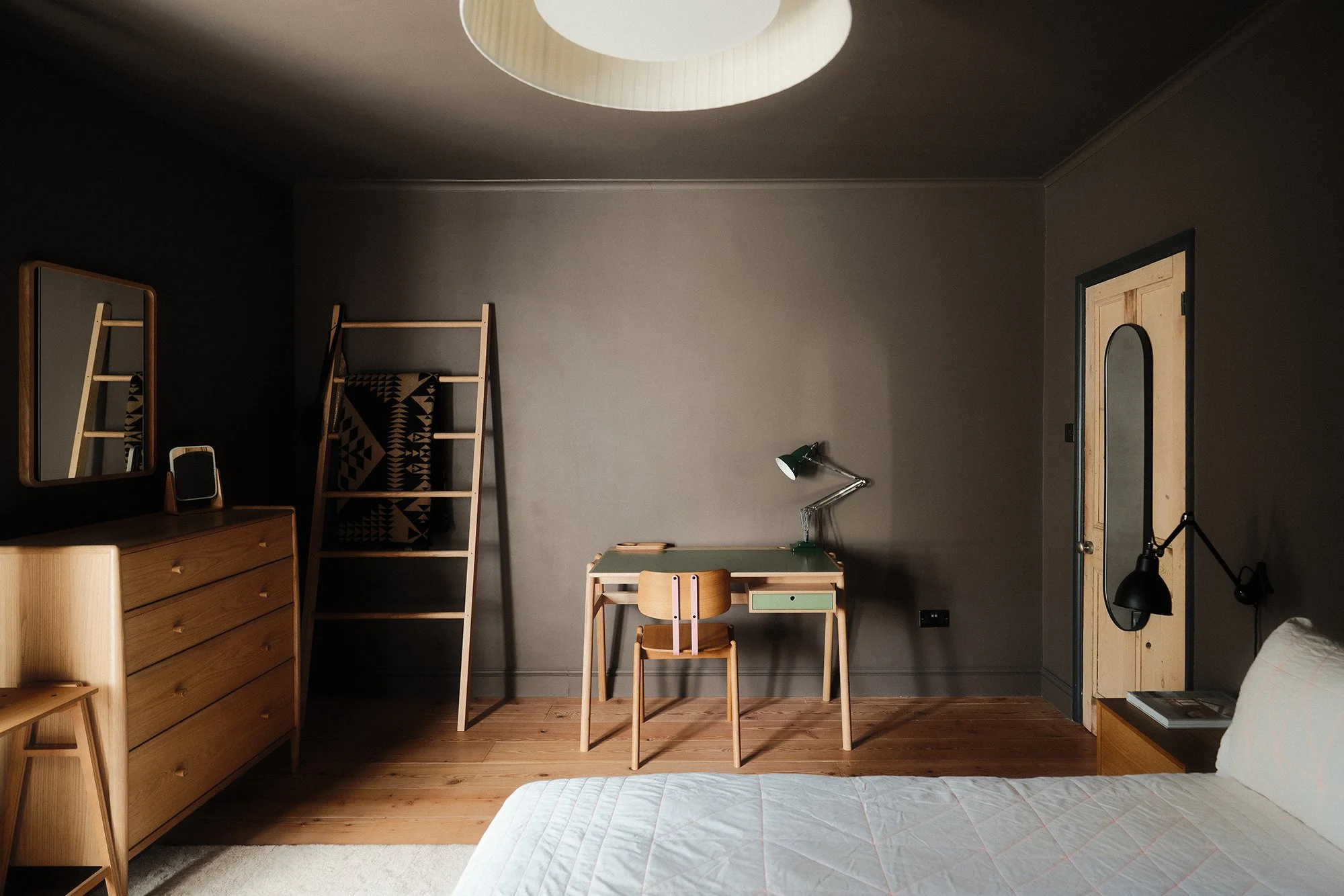 Interior view of a modern kitchen with wooden cabinets, a green accent wall, and a white countertop. There is a window above the sink and a door opening to an outdoor area with brick walls.