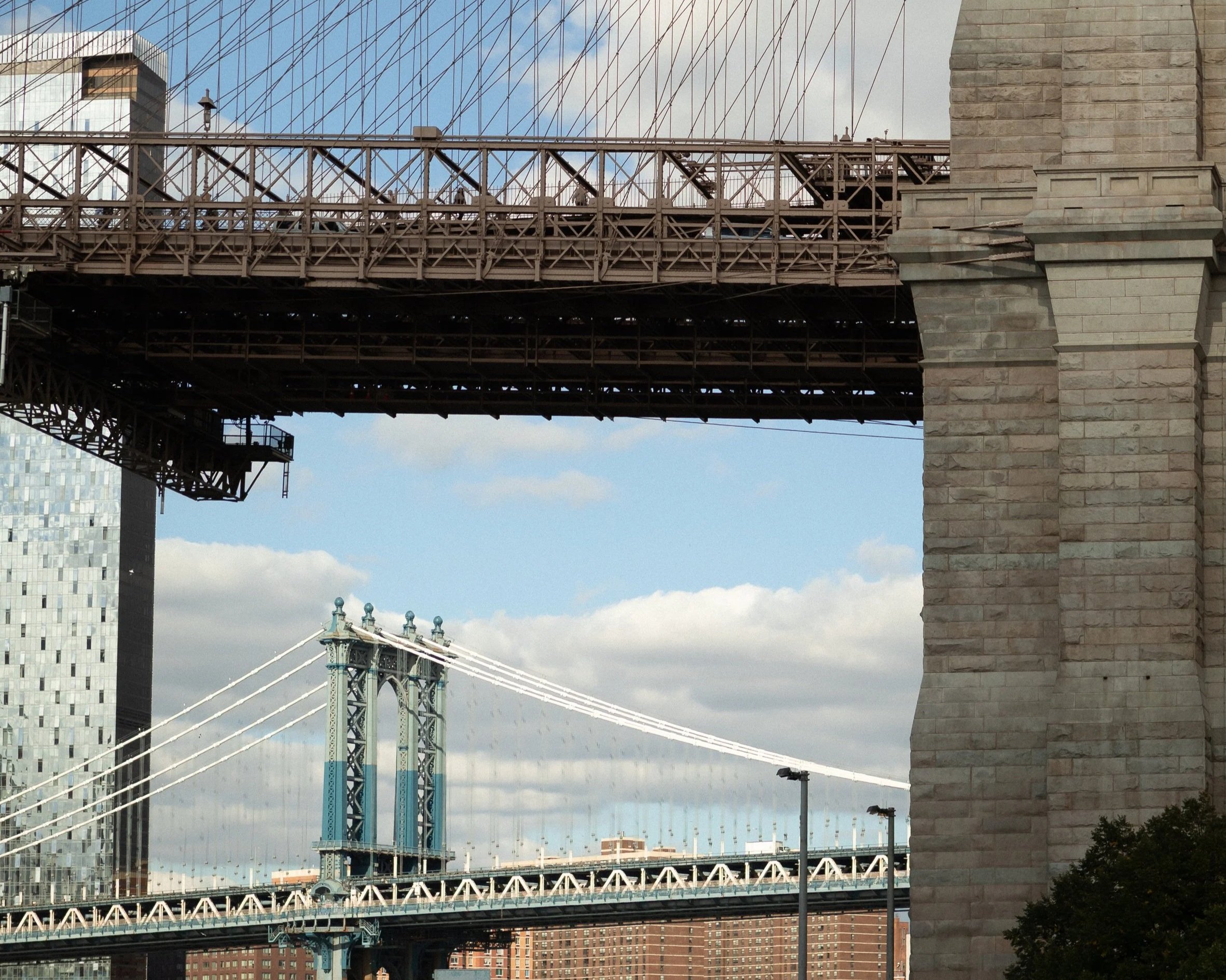 View of three bridges in New York City, including the Brooklyn Bridge and Manhattan Bridge under a partly cloudy sky.