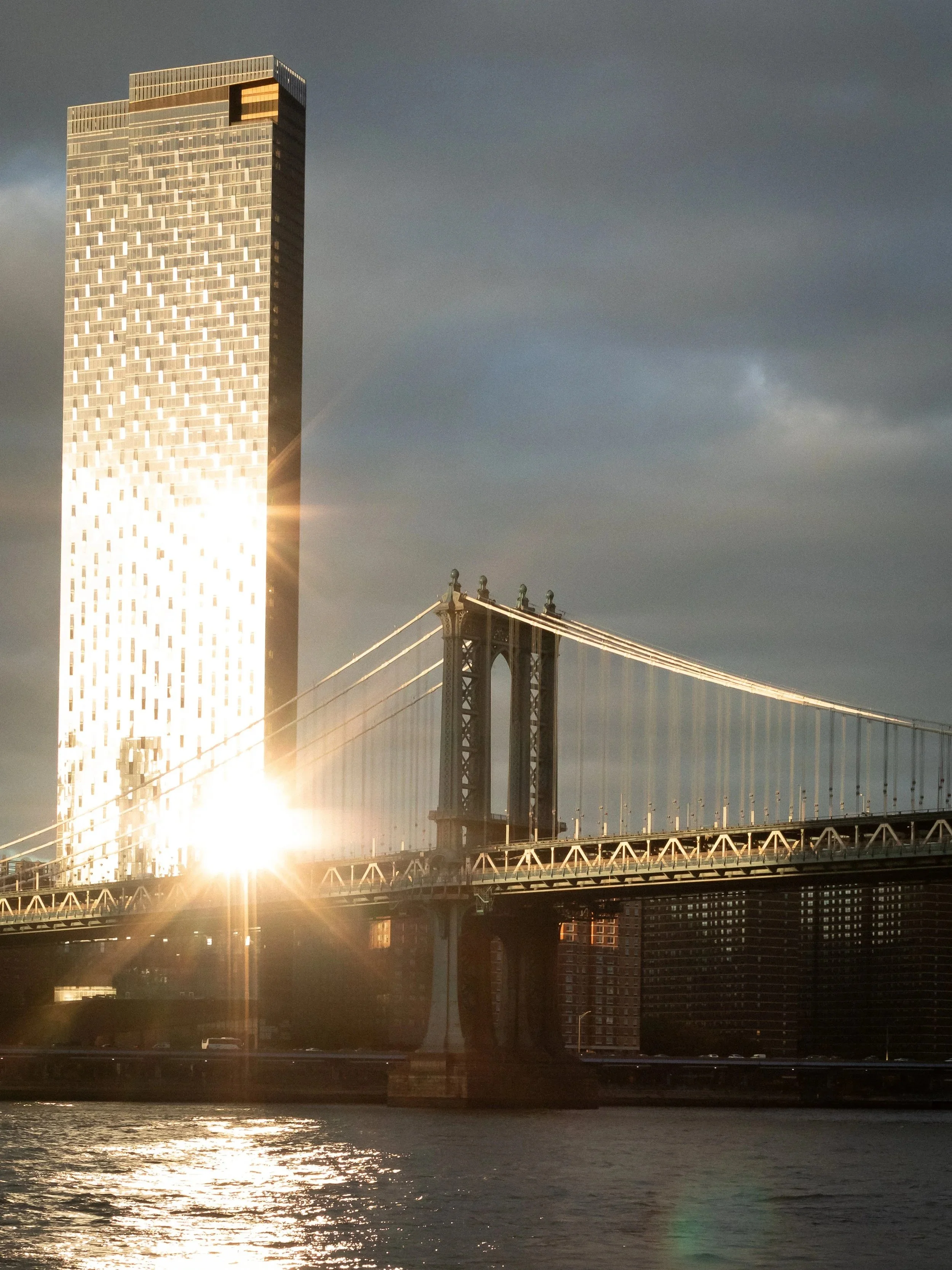 Sunset over a cityscape featuring a modern high-rise building with reflective glass windows and a bridge over a river.