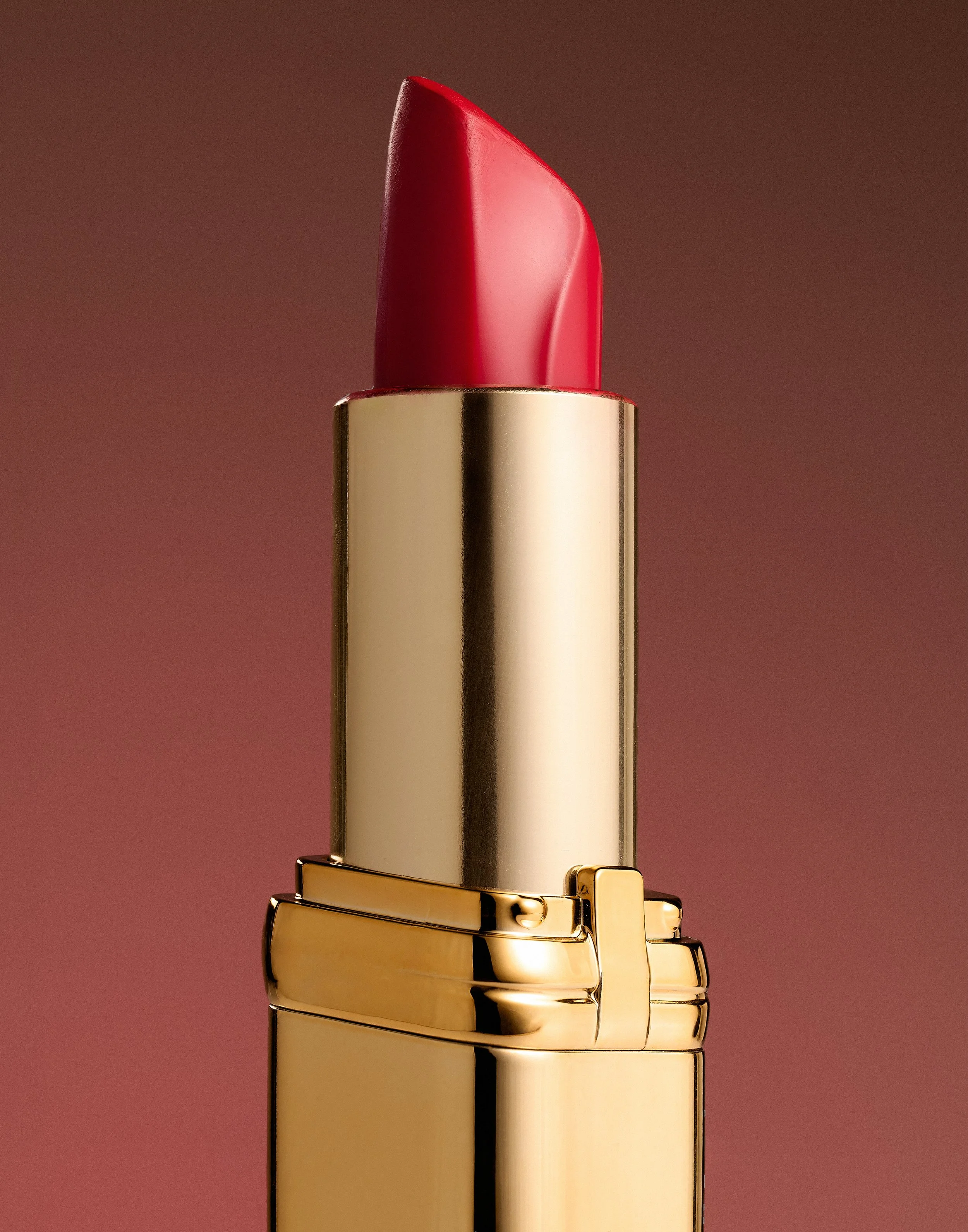 Close-up of a red lipstick in a gold tube against a pink background.