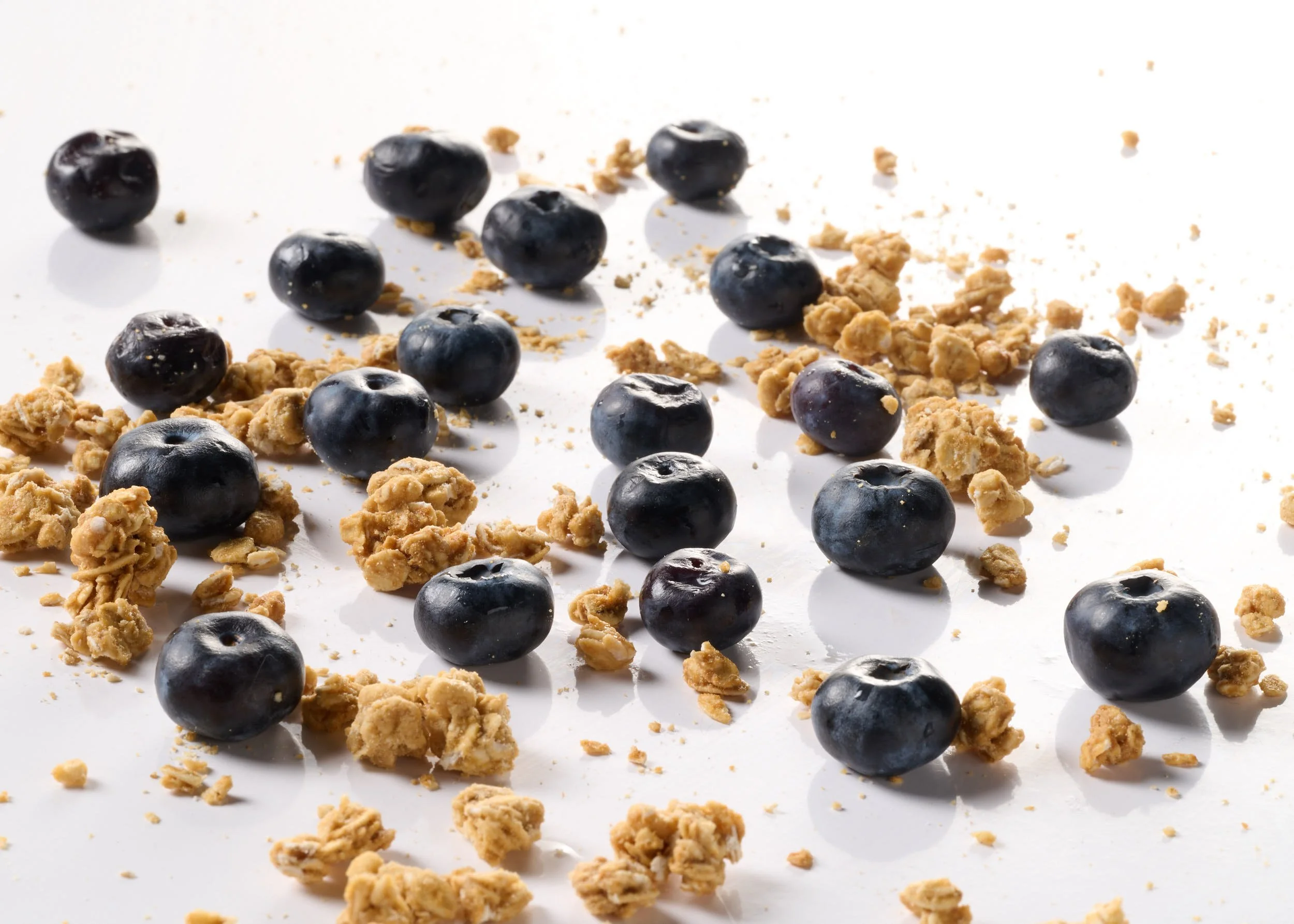 Blueberries and crumbled granola scattered on a white surface.