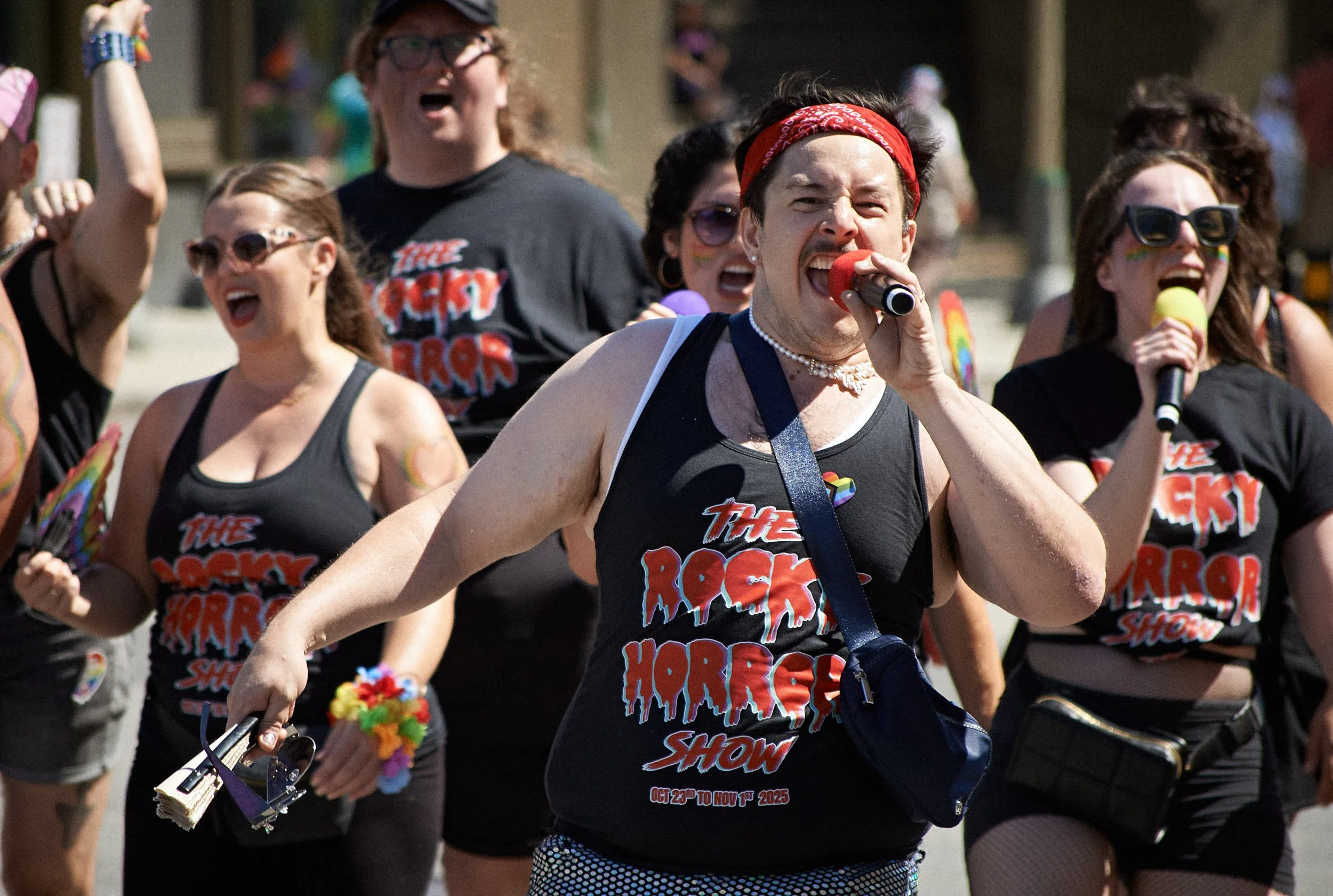 A group of people participating in a pride parade, wearing matching black T-shirts with 