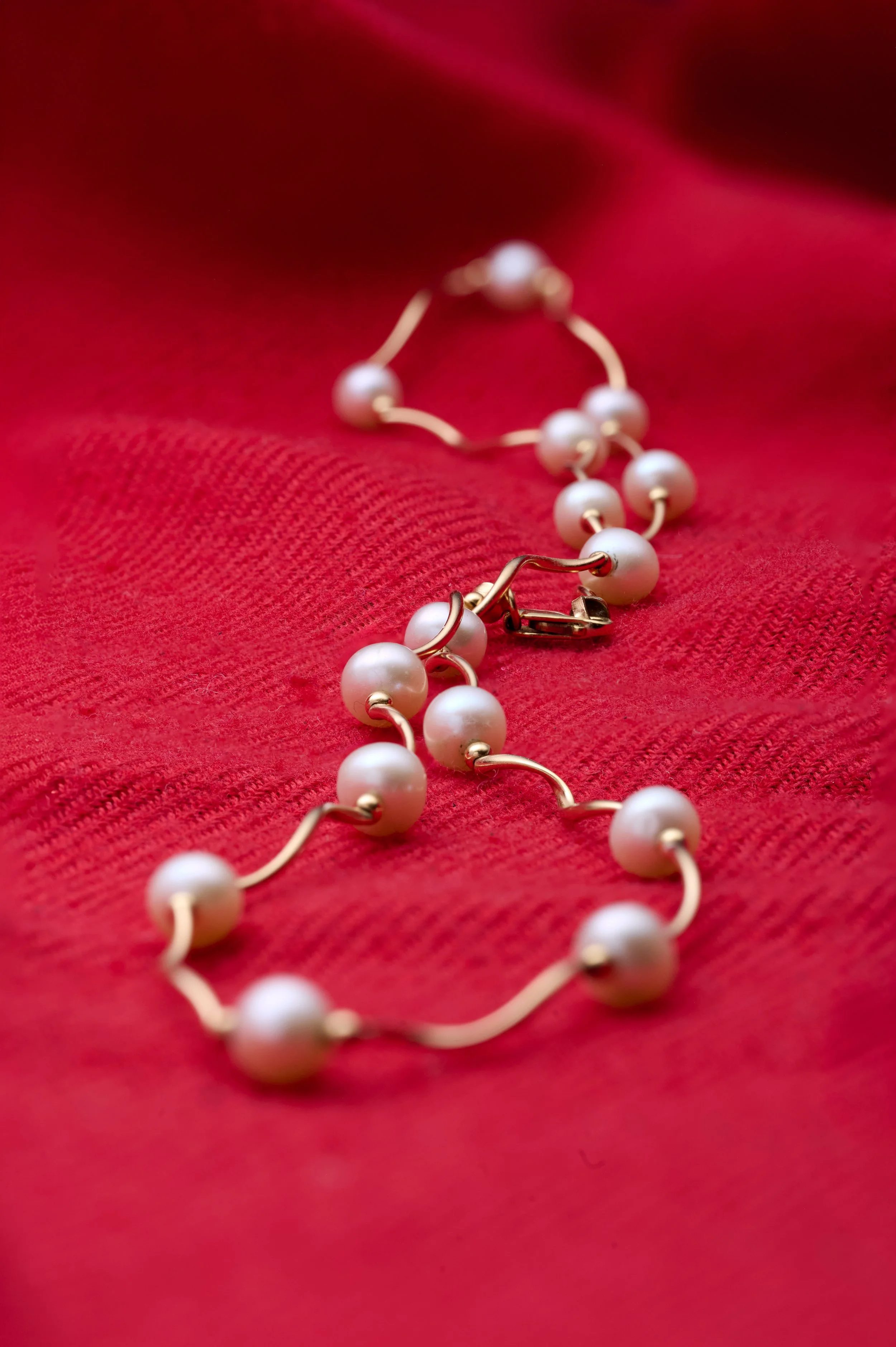 Pearl necklace with gold clasp placed on red textured fabric.