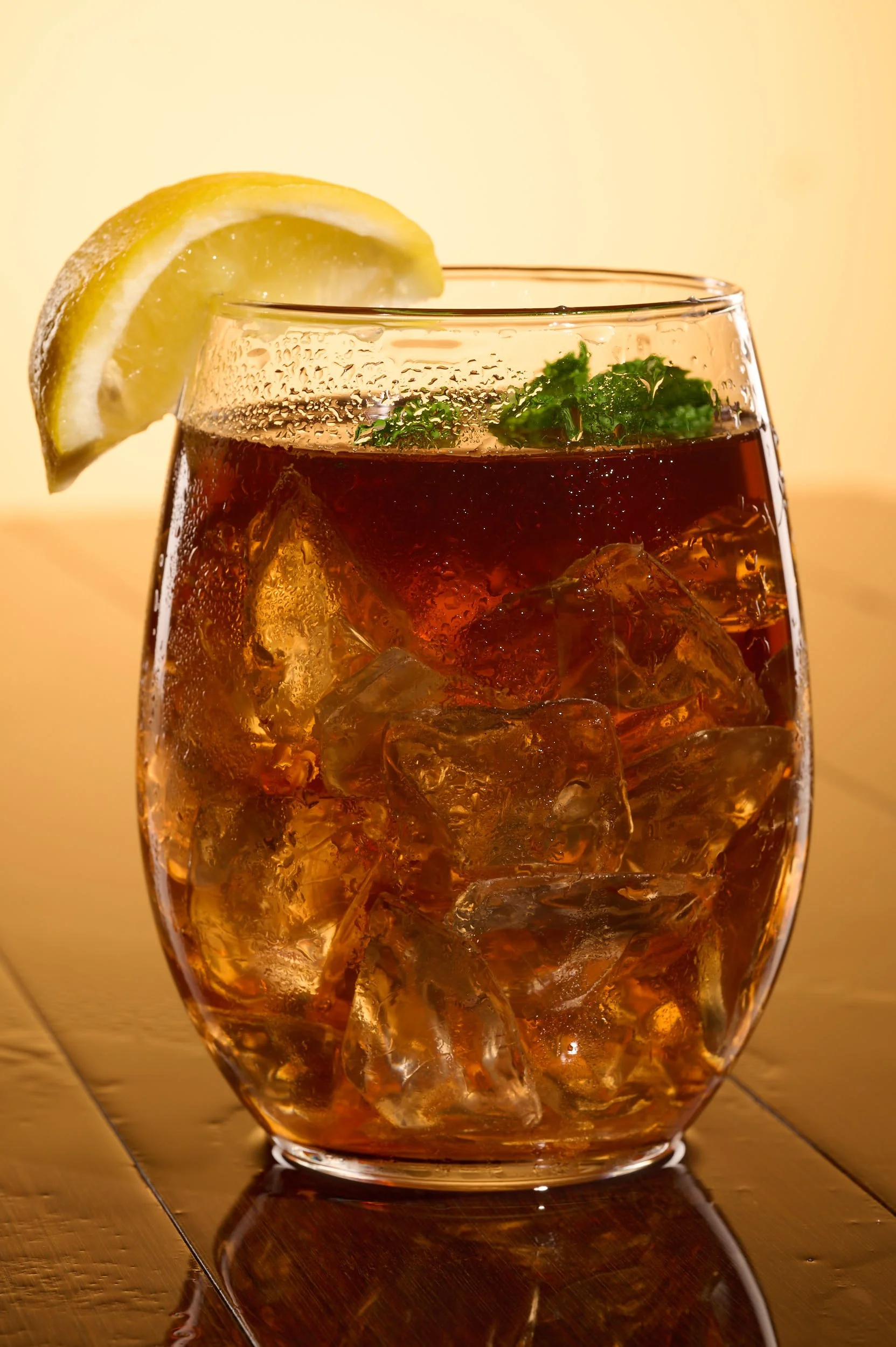 A glass of iced tea garnished with a lemon wedge and a sprig of mint.